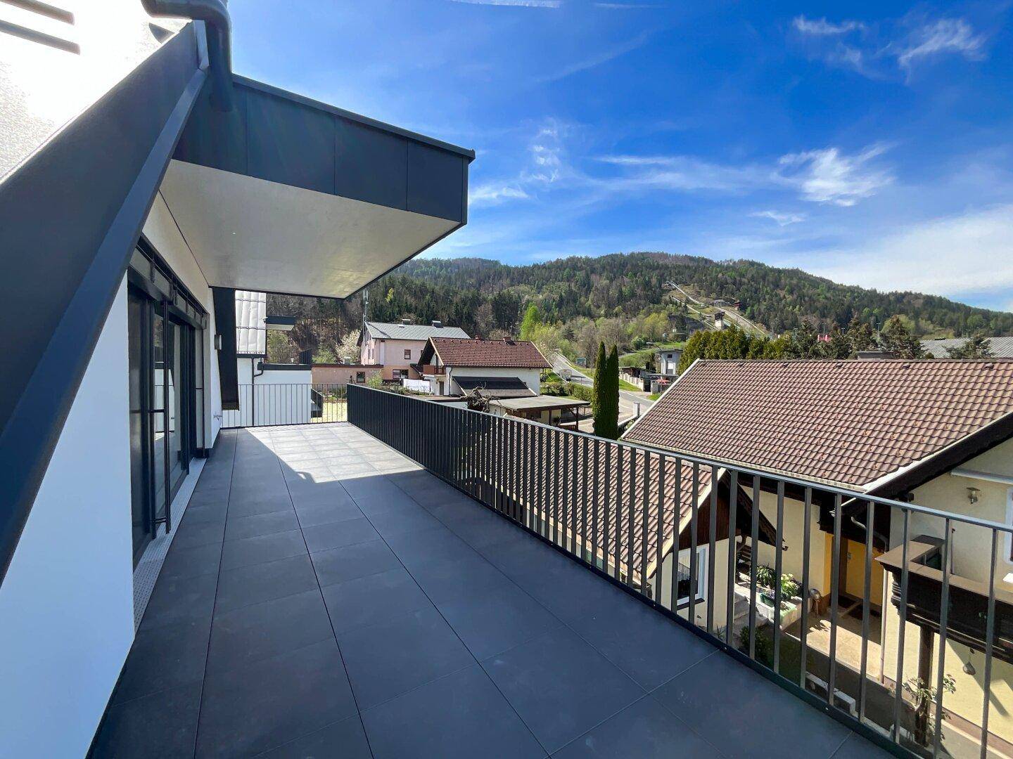 Geräumiger Balkon mit dunklen Fliesen und Metallgeländer, bietet Blick auf die umliegende Landschaft.