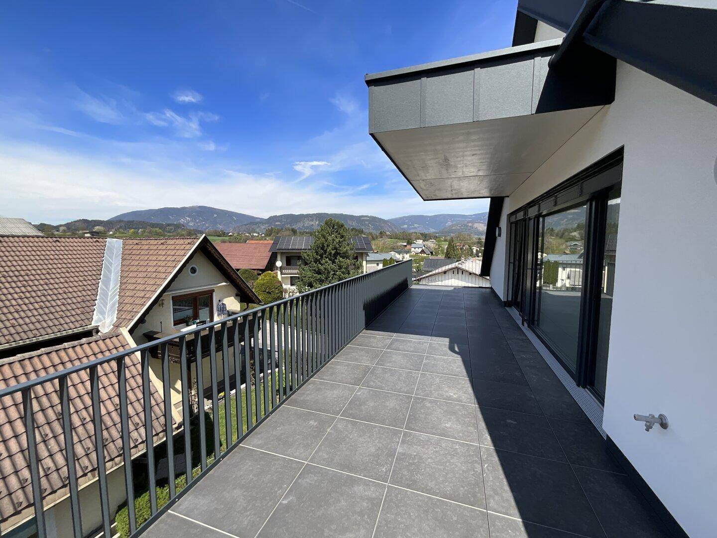 Langer Balkon mit modernen Fliesen und weitem Blick über die Dächer und grüne Hügel.
