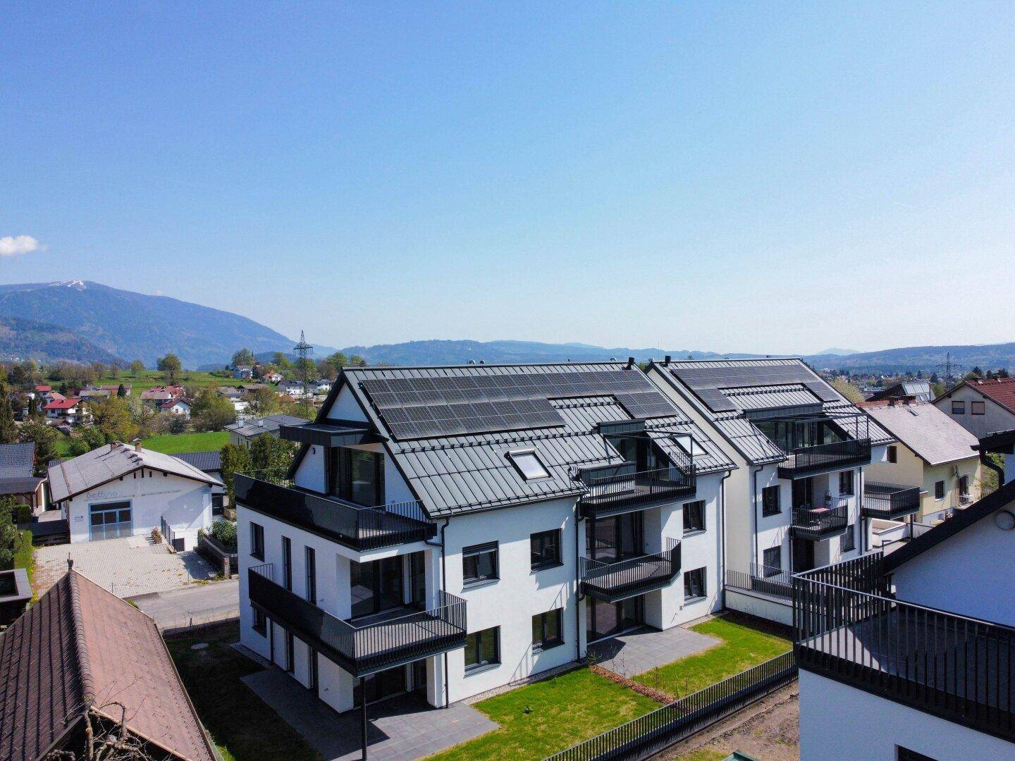 Luftaufnahme einer modernen Wohnanlage mit Solarpaneelen auf den Dächern und Bergblick.