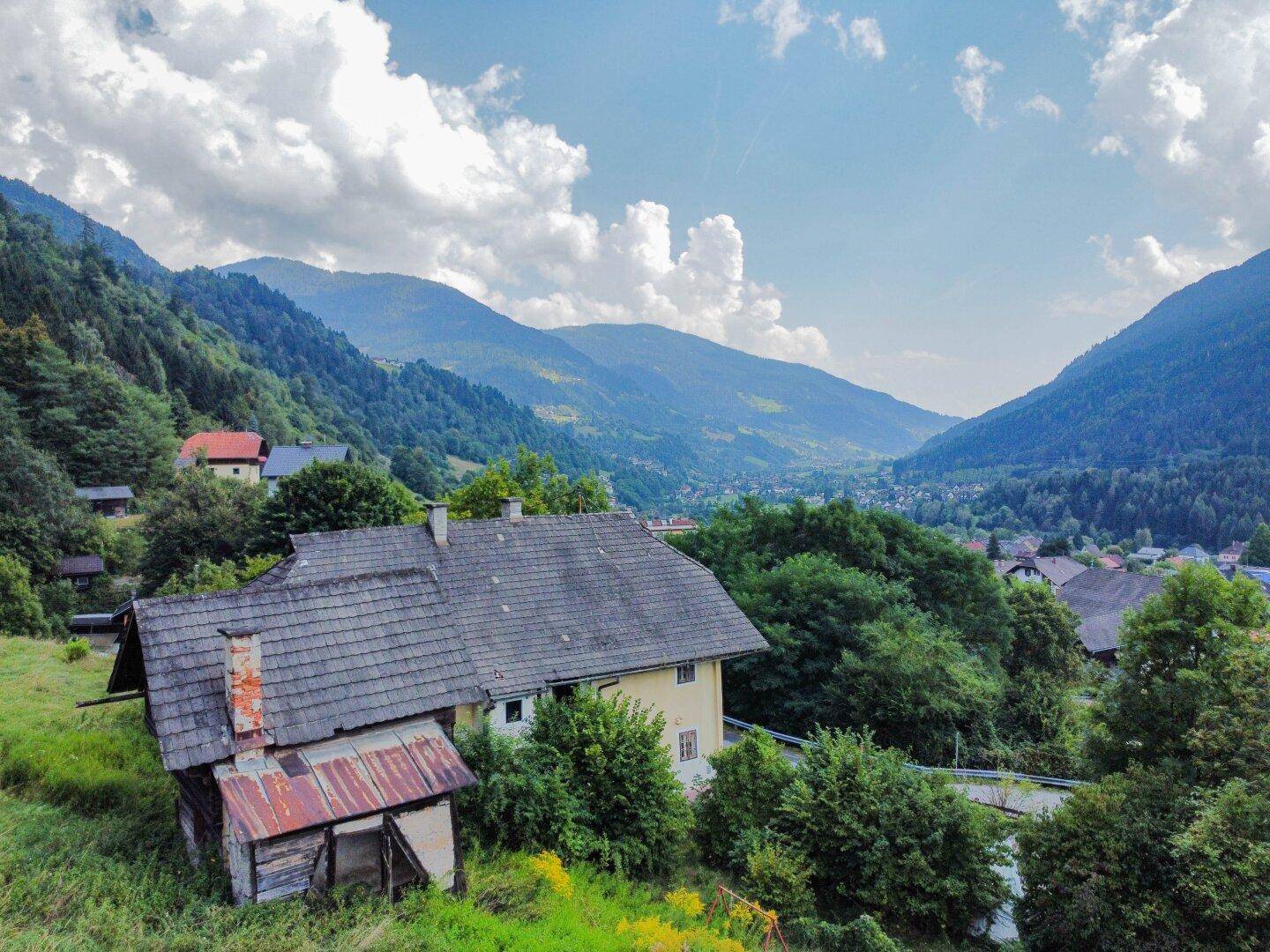 Rückansicht des Hauses mit Blick auf das Tal und die umliegenden Berge unter blauem Himmel.