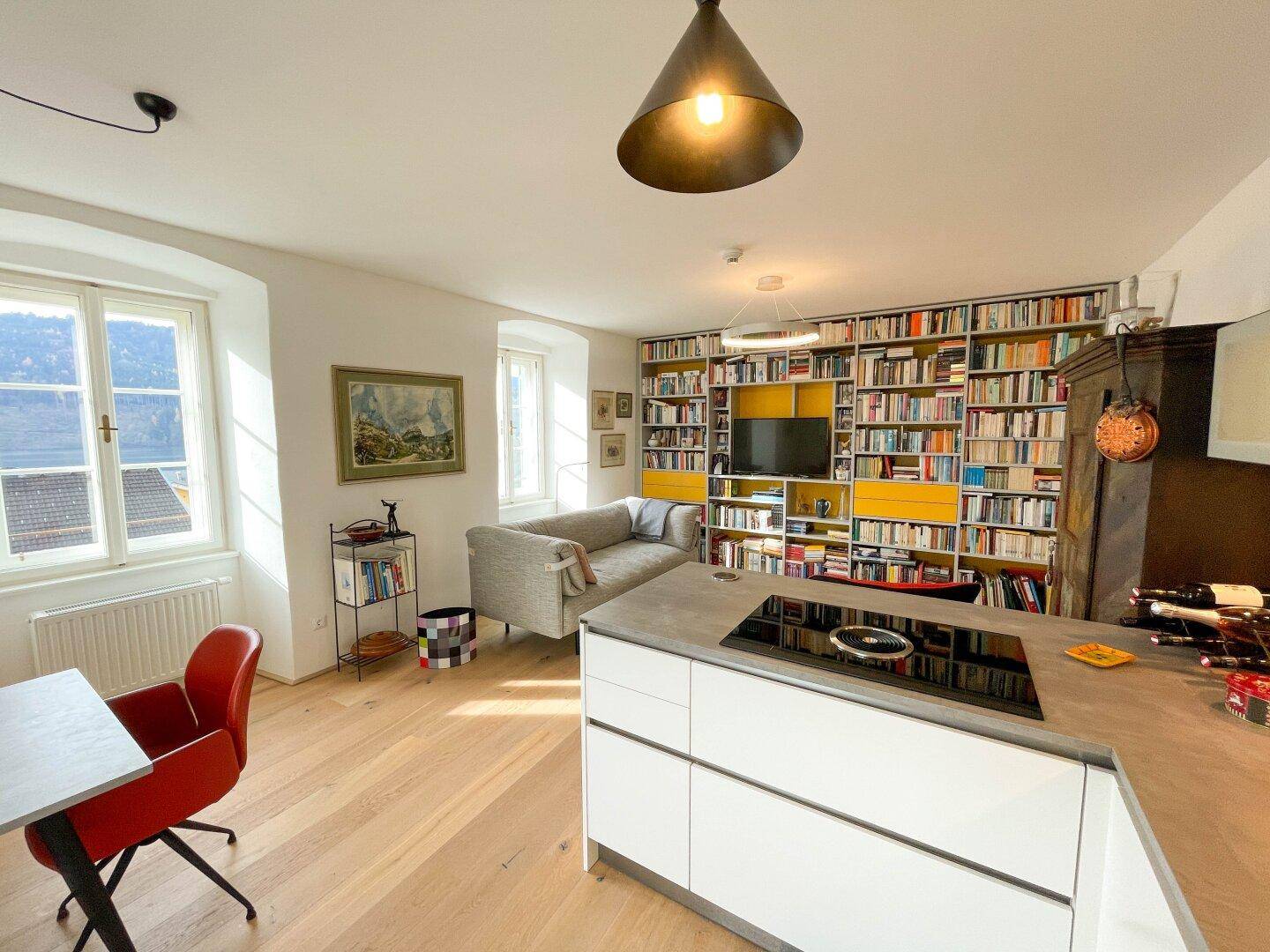 Moderner Wohnbereich mit Kücheninsel, Induktionskochfeld und einer beeindruckenden Bücherwand mit integriertem Fernseher.