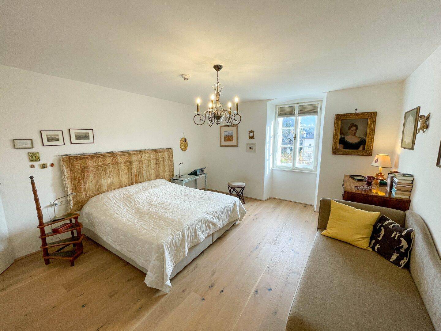 Gemütliches Schlafzimmer mit Holzboden, großem Bett und einem Fenster, das viel natürliches Licht hereinlässt.