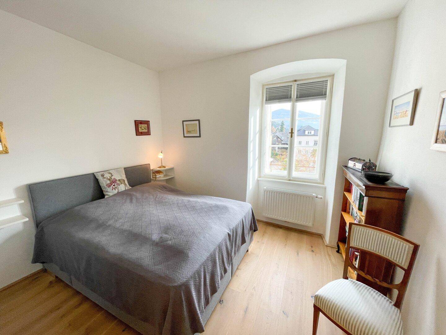 Helles Schlafzimmer mit Holzboden, Doppelbett und einem Fenster mit Blick auf die umliegende Landschaft.