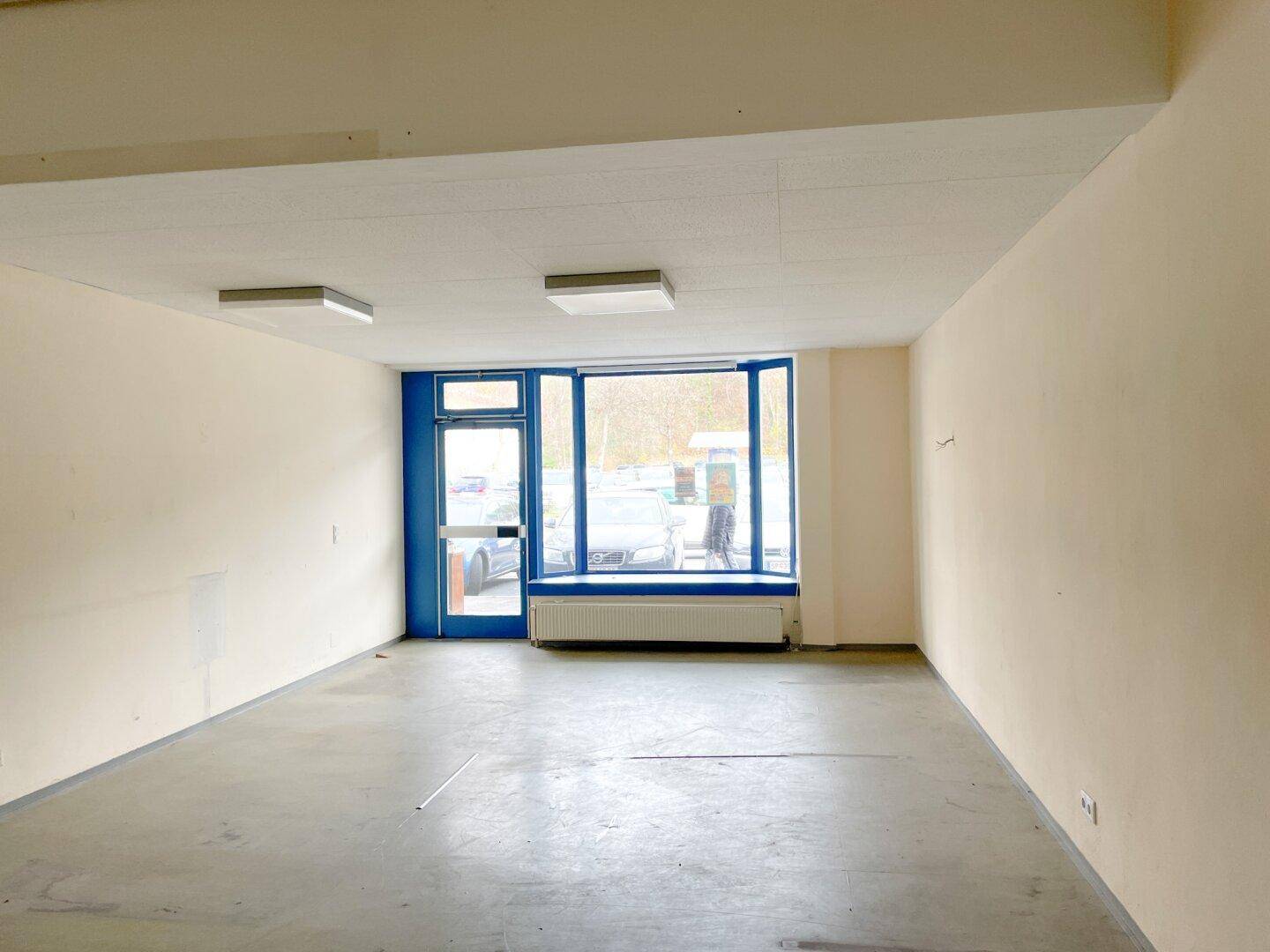 Heller Gewerberaum mit großen Fenstern zur Straße und funktionaler Deckenbeleuchtung.