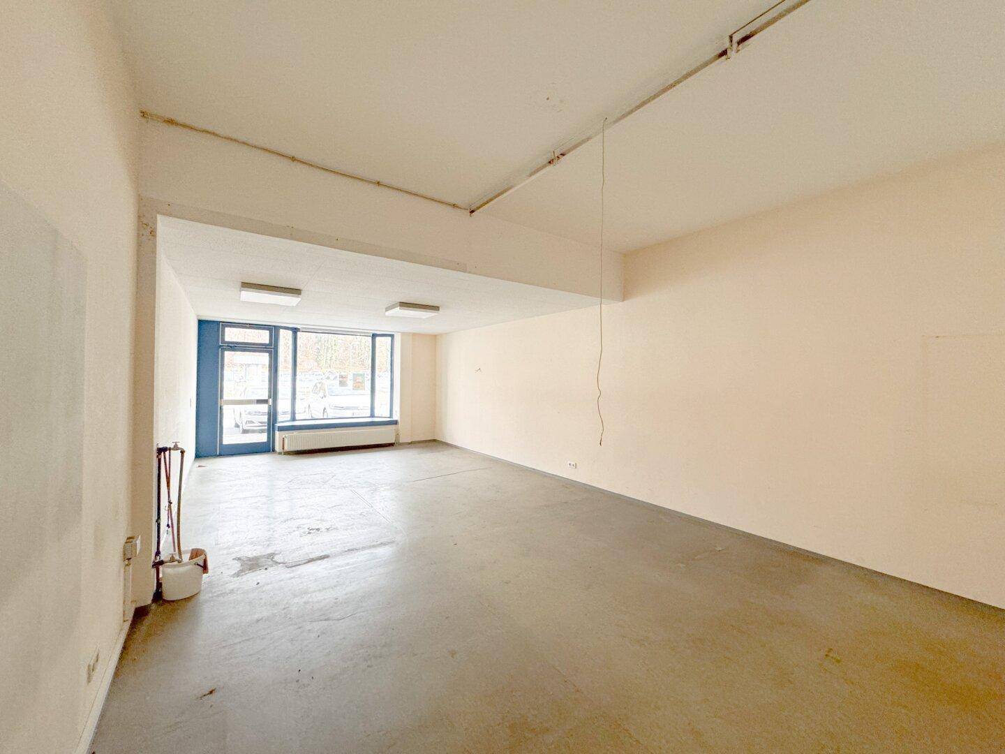 Weitläufiger Gewerberaum mit großen Fenstern und einfacher Deckenbeleuchtung, ideal für Ladenflächen.