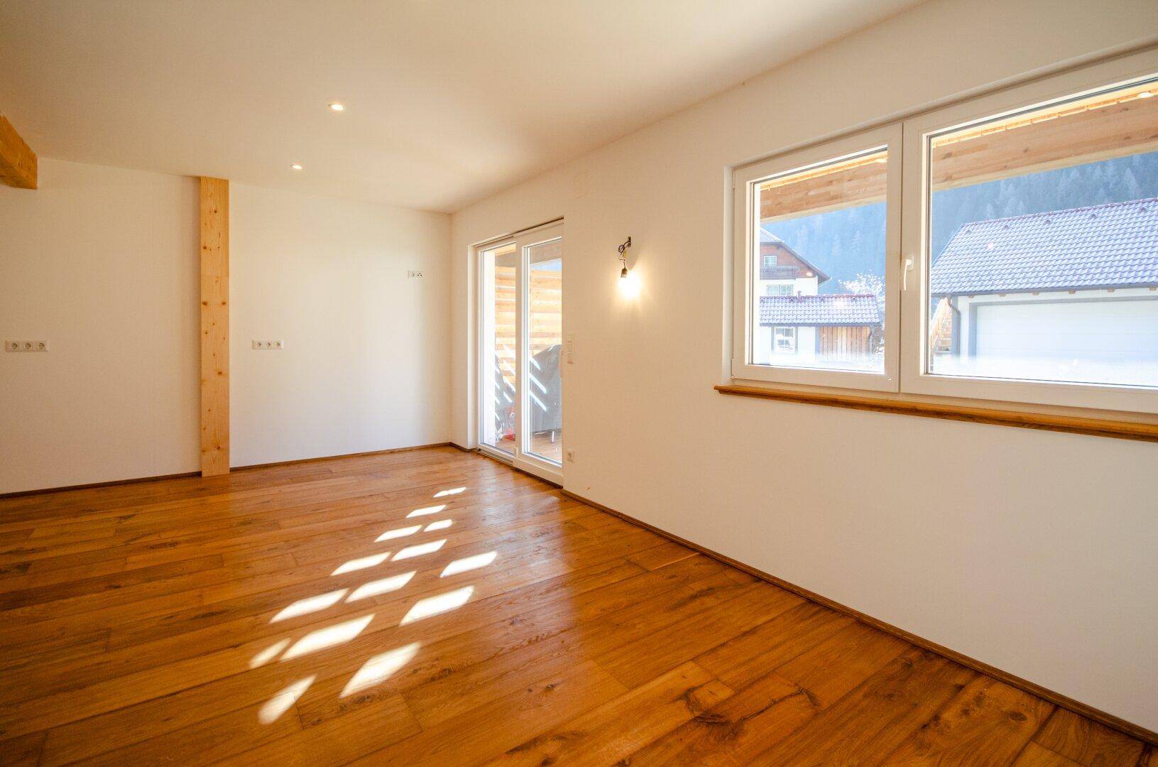 Lichtdurchfluteter Raum mit Holzboden, großen Fenstern und Blick auf die Berge.