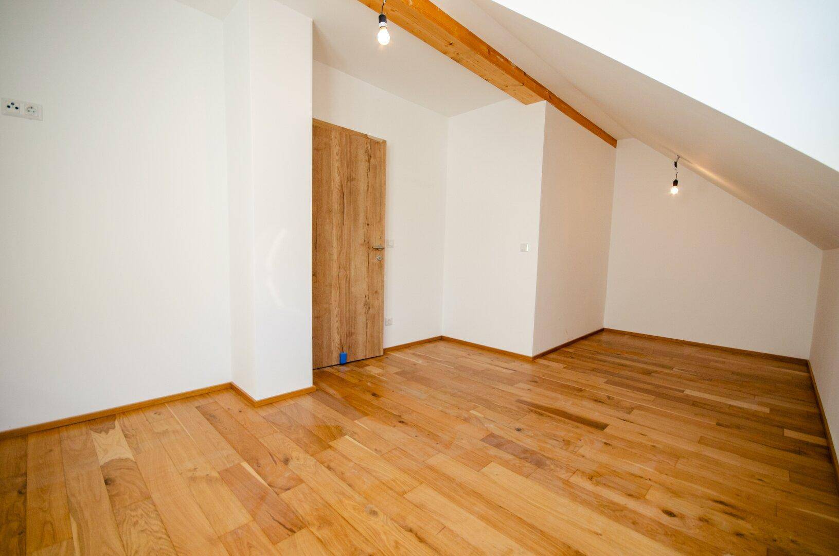 Dachgeschosszimmer mit Holzboden, schrägen Wänden und sichtbaren Holzbalken.