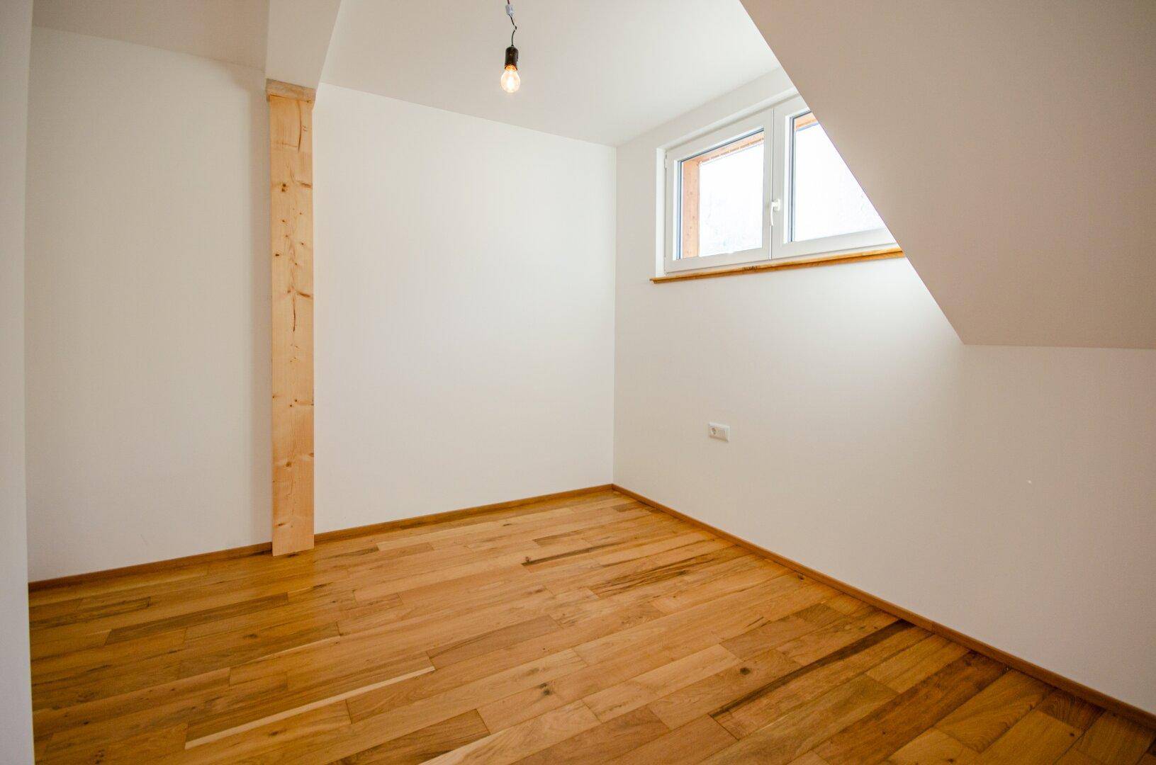 Helles Schlafzimmer im Dachgeschoss mit Holzboden, schrägen Wänden und einem Fenster.