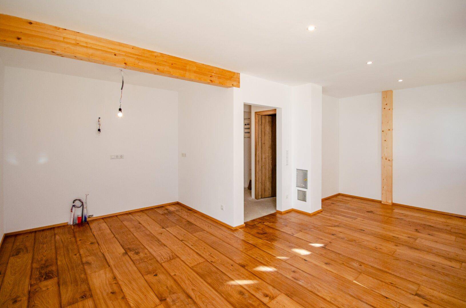 Geräumiger, heller Raum mit Holzboden und sichtbaren Holzbalken, bereit zur Einrichtung.