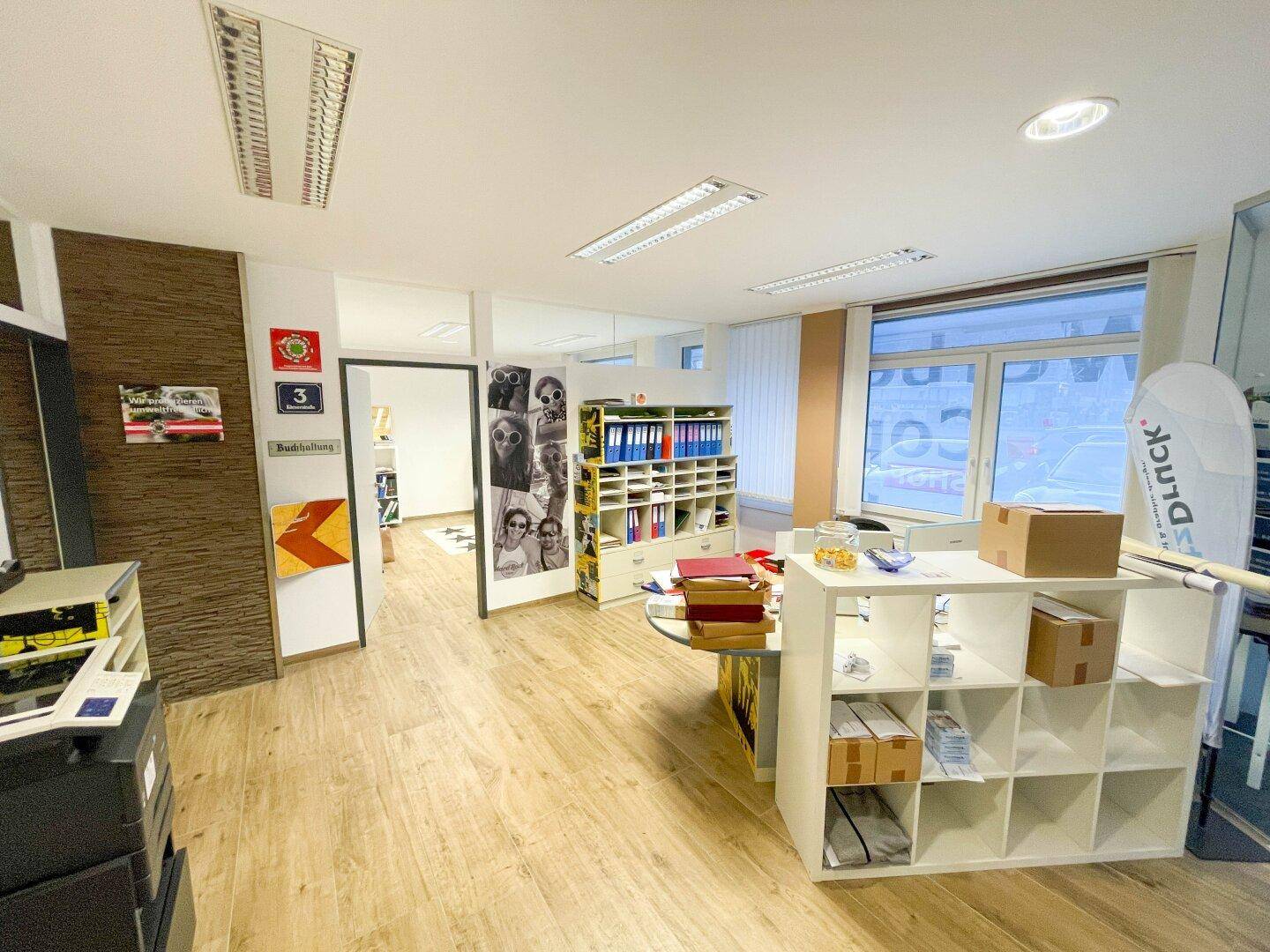 Geräumiges Büro mit Holzfußboden, Regalen und viel Tageslicht durch große Fenster.