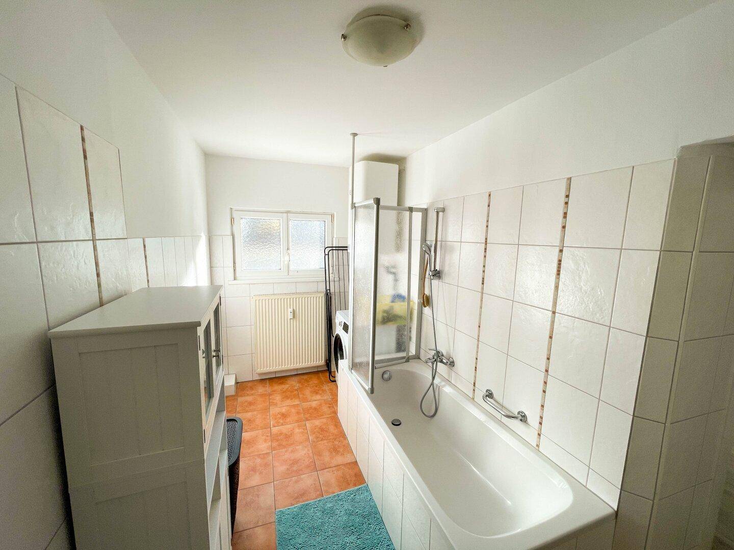 Badezimmer mit Badewanne, Duschabtrennung, Fliesenboden und einem Fenster.