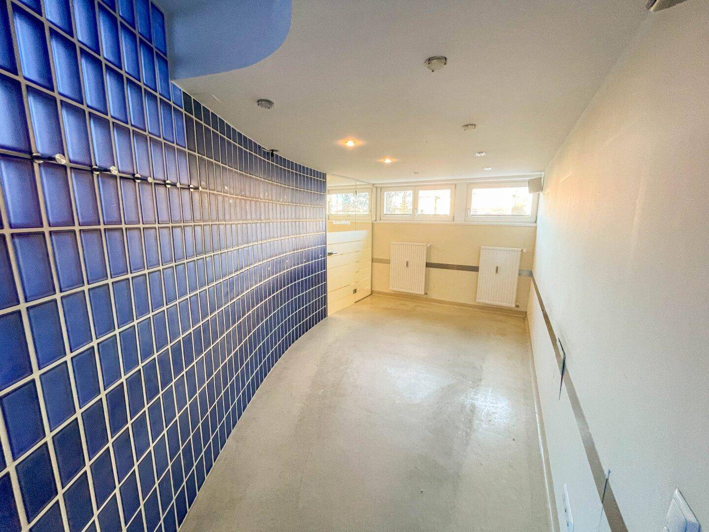Flur mit auffälliger blauer Fliesenwand und kleinen Fenstern, die Tageslicht hereinlassen.