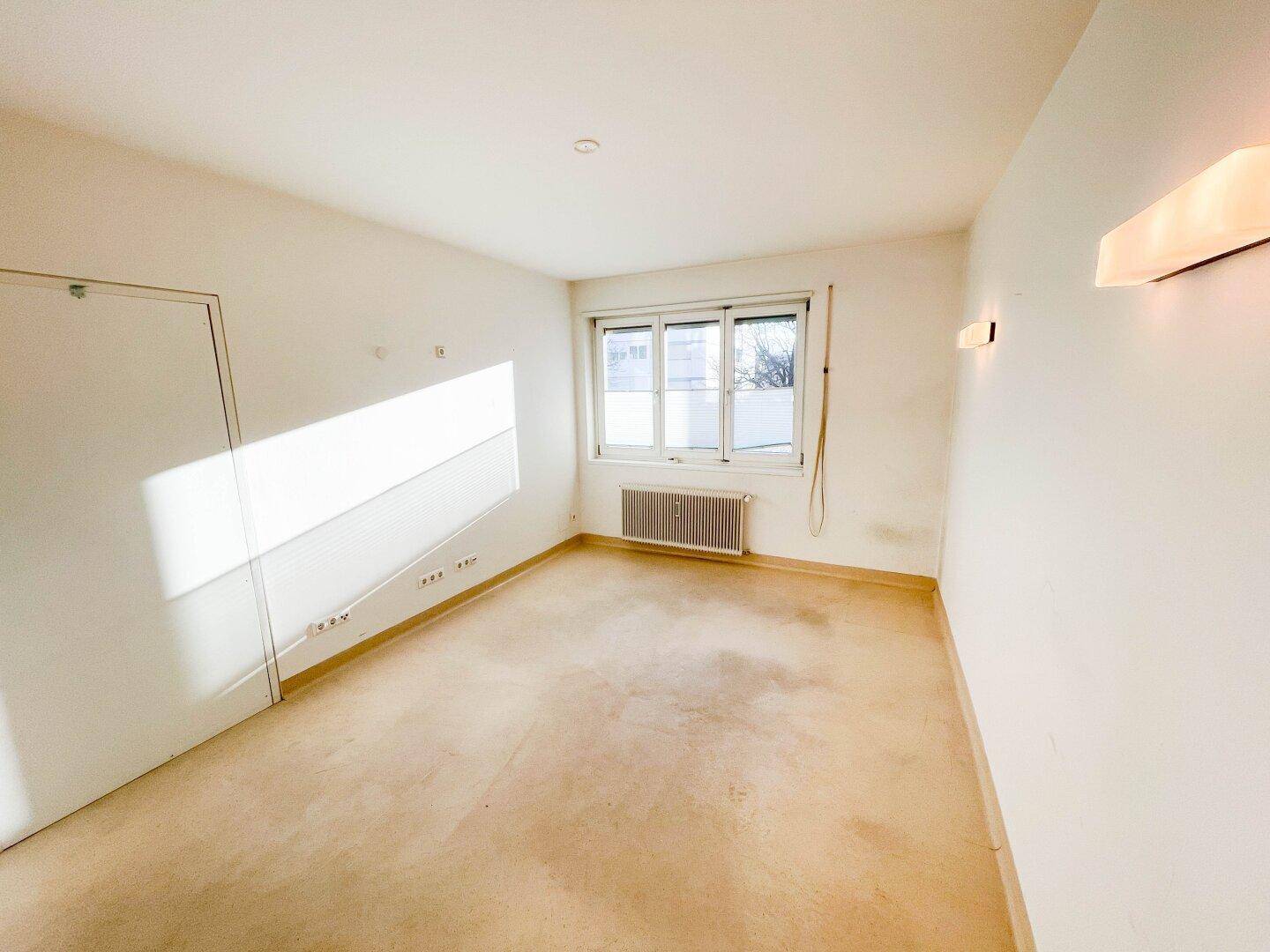 Kleiner Büroraum mit Teppichboden, Fenster und Wandleuchten, ideal für Einzelbüro oder Arbeitszimmer.