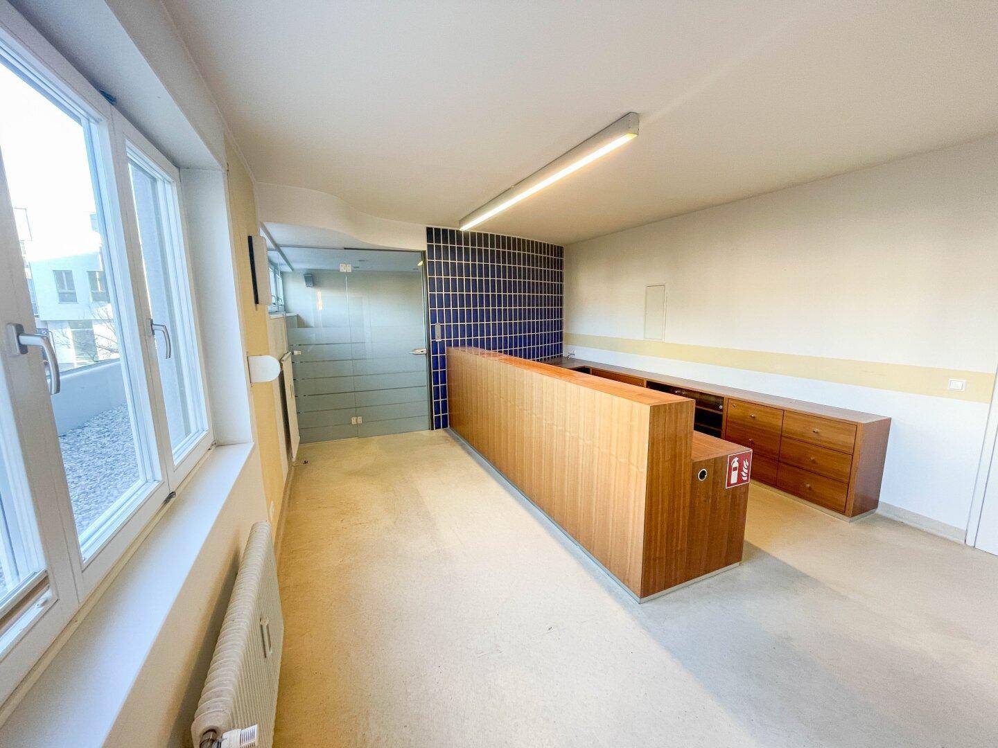 Heller Empfangsbereich mit Holztheke, blauer Fliesenwand und großen Fenstern, sehr einladend.