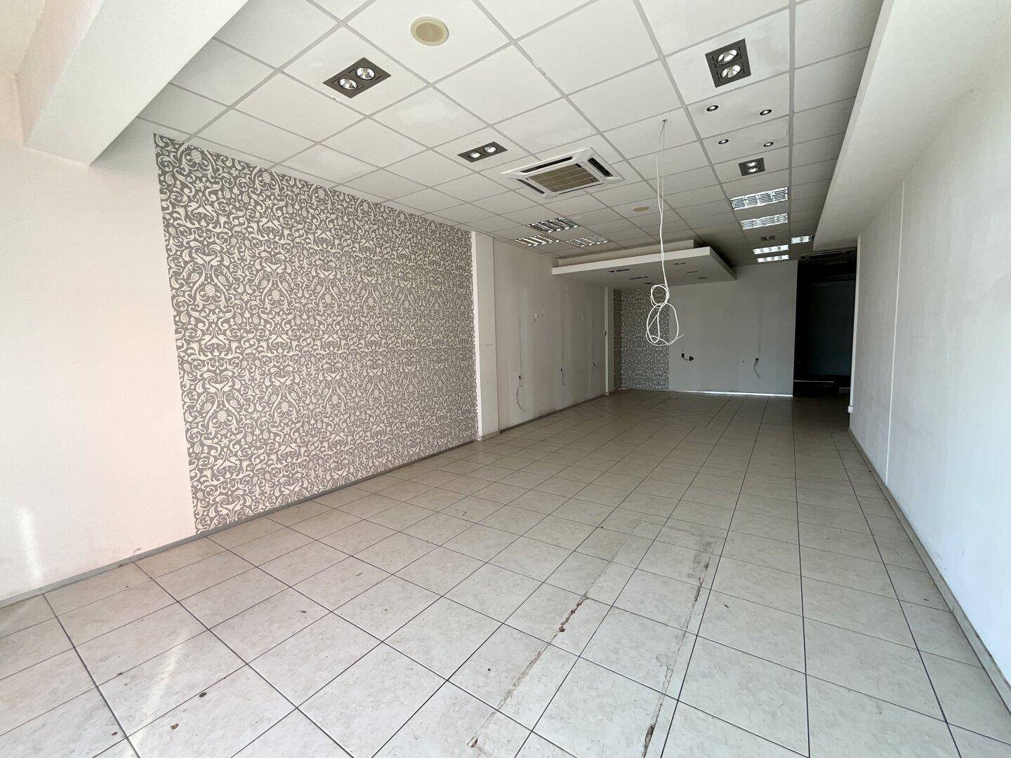 Geräumiger Ladenbereich mit gemusterter Wand, Fliesenboden und moderner Deckenbeleuchtung.