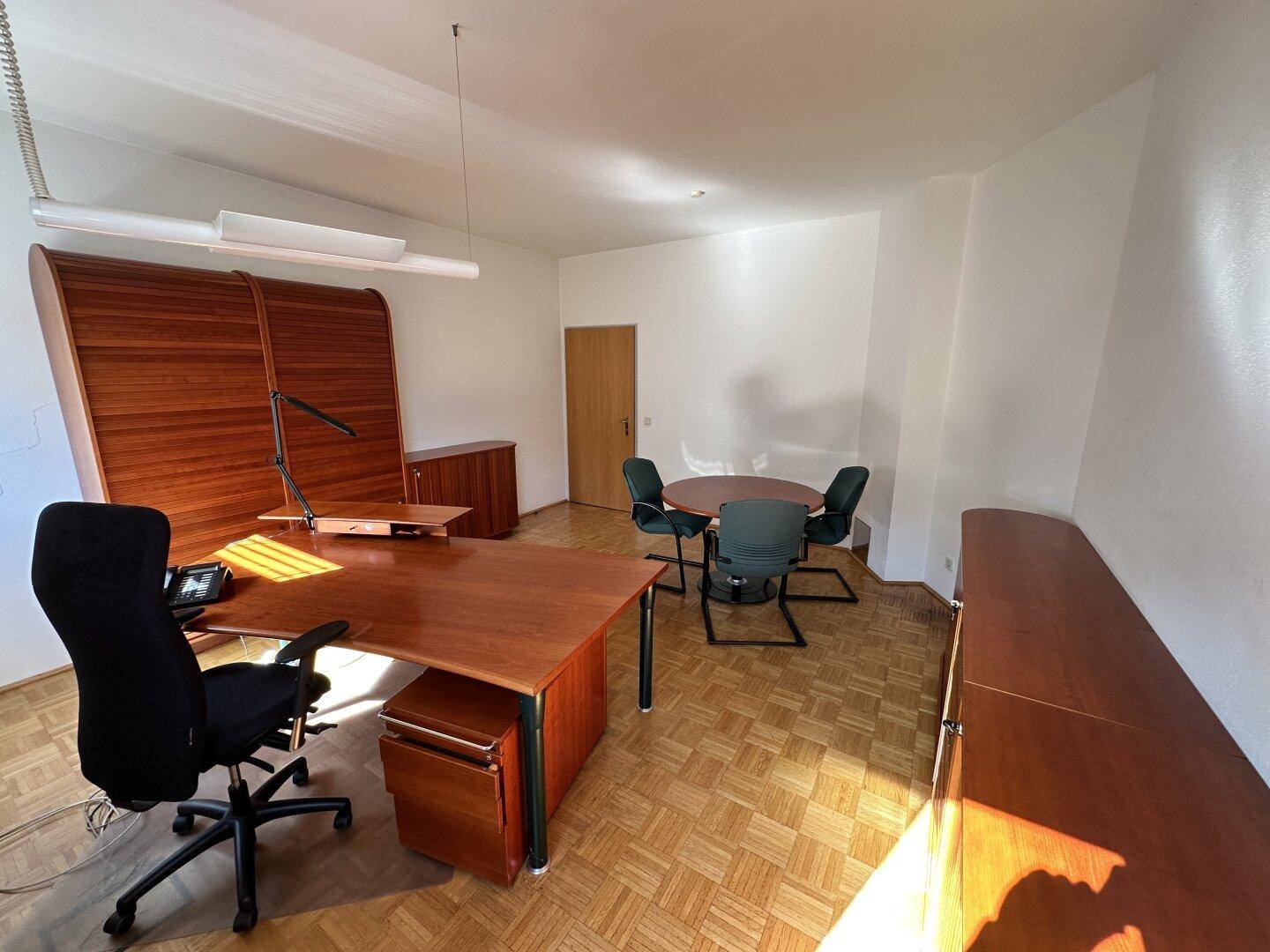 Helles Büro mit modernem Holzschreibtisch, Besprechungsbereich und viel Tageslicht.