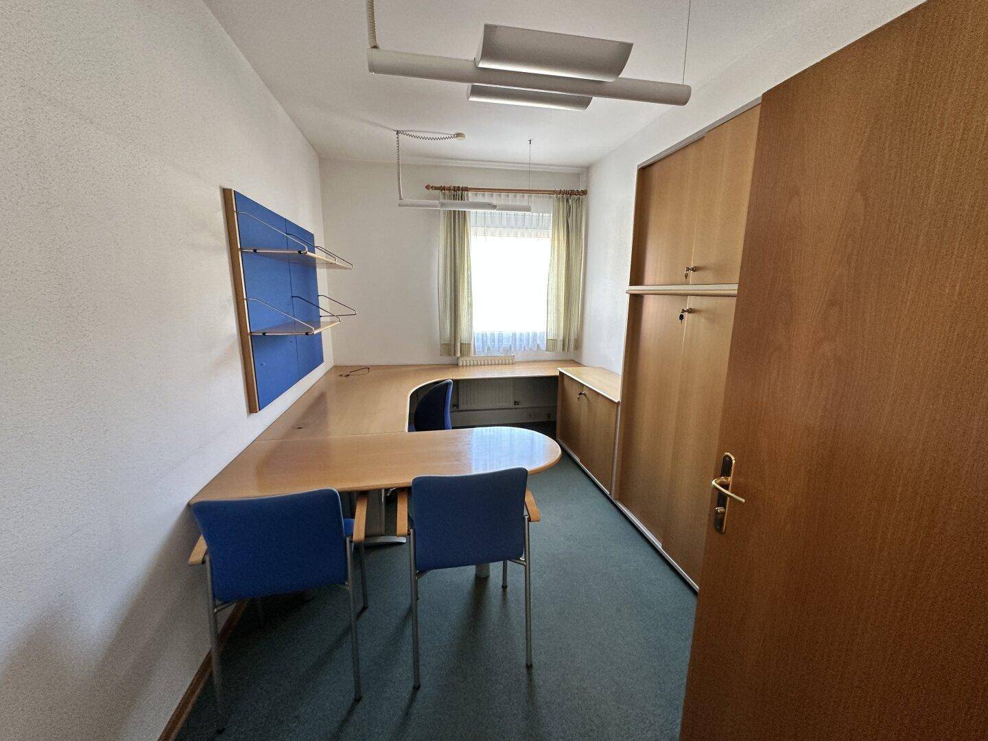 Kleineres Büro mit U-förmigem Schreibtisch, blauen Stühlen und Teppichboden, ideal für Einzelarbeit.