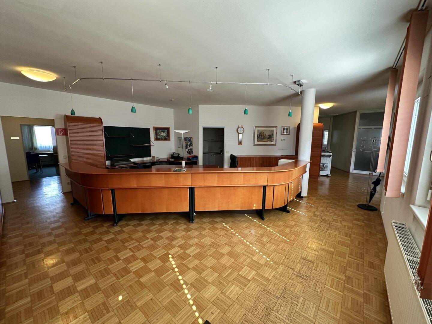 Großer Empfangsbereich mit geschwungener Holztheke und Parkettboden in einem Bürogebäude.