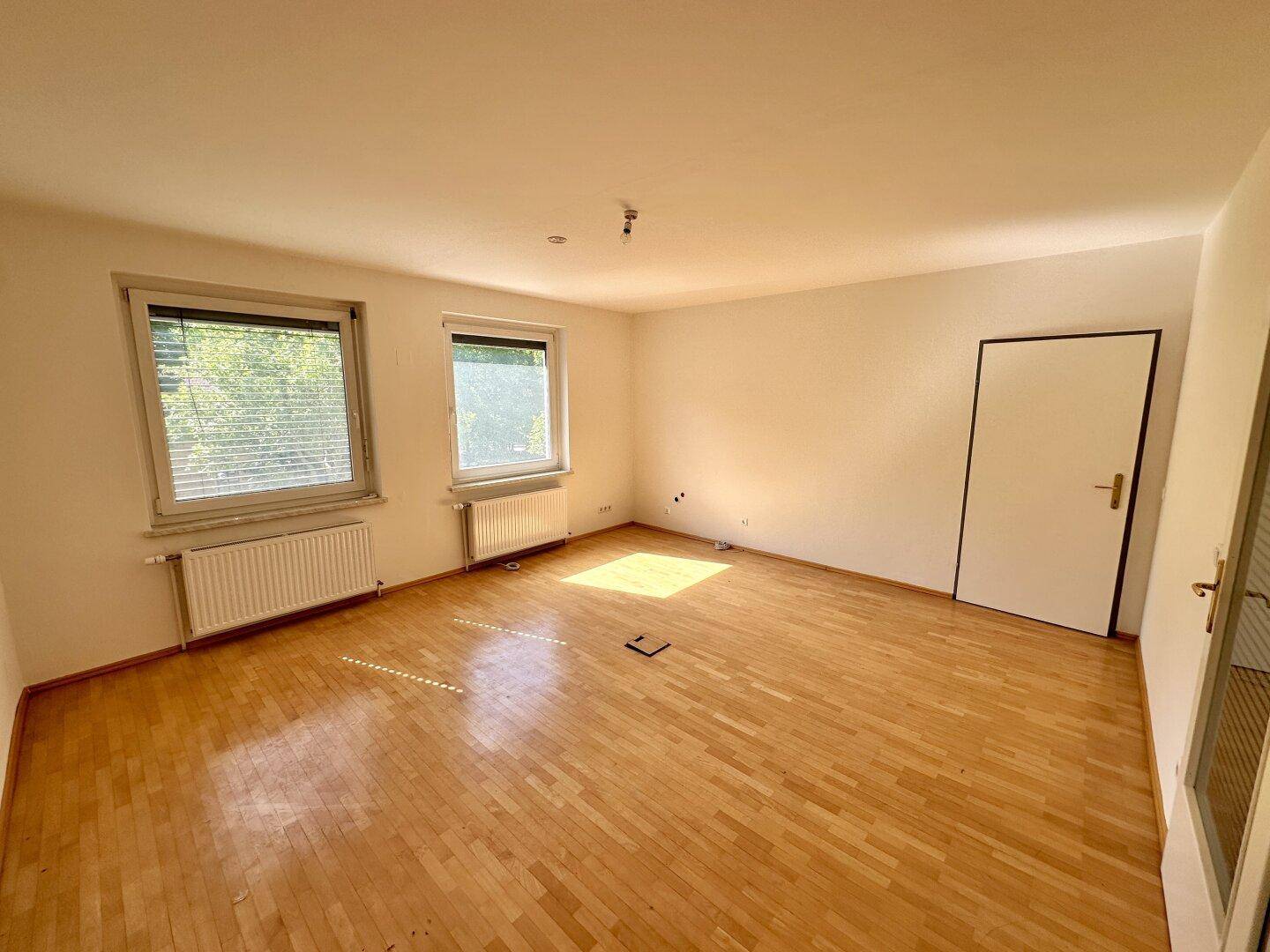 Geräumiger, heller Raum mit Holzboden und zwei Fenstern, die viel Sonnenlicht hereinlassen, ideal für flexible Nutzung.