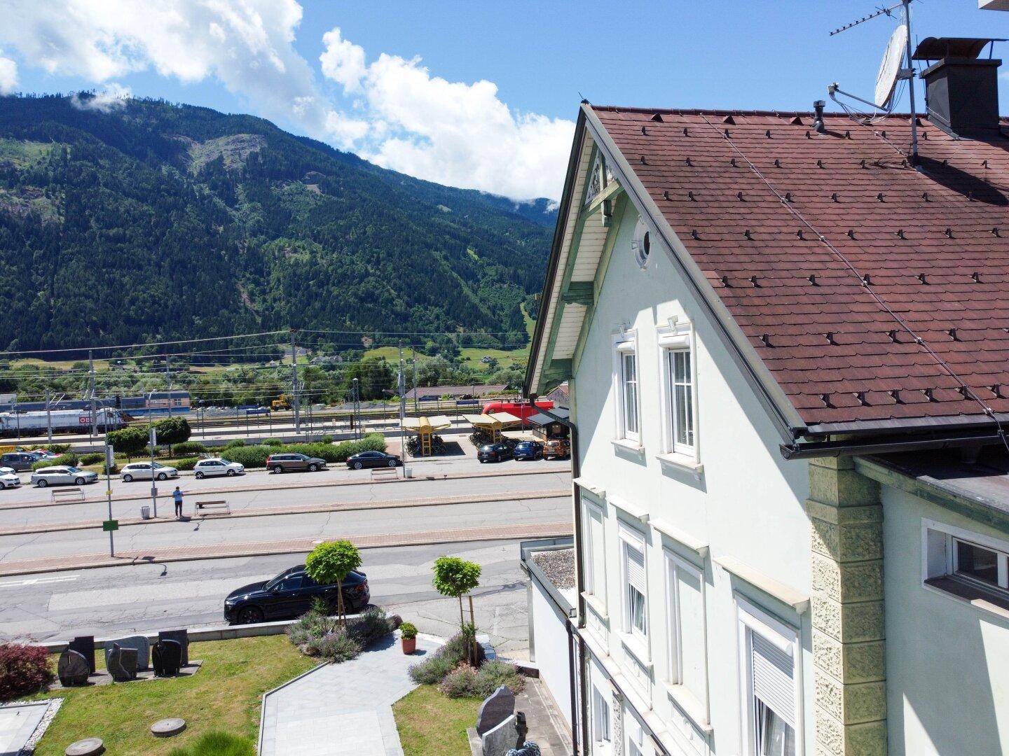 Blick auf die umliegende Berglandschaft und die Straße mit vorbeifahrenden Zügen.