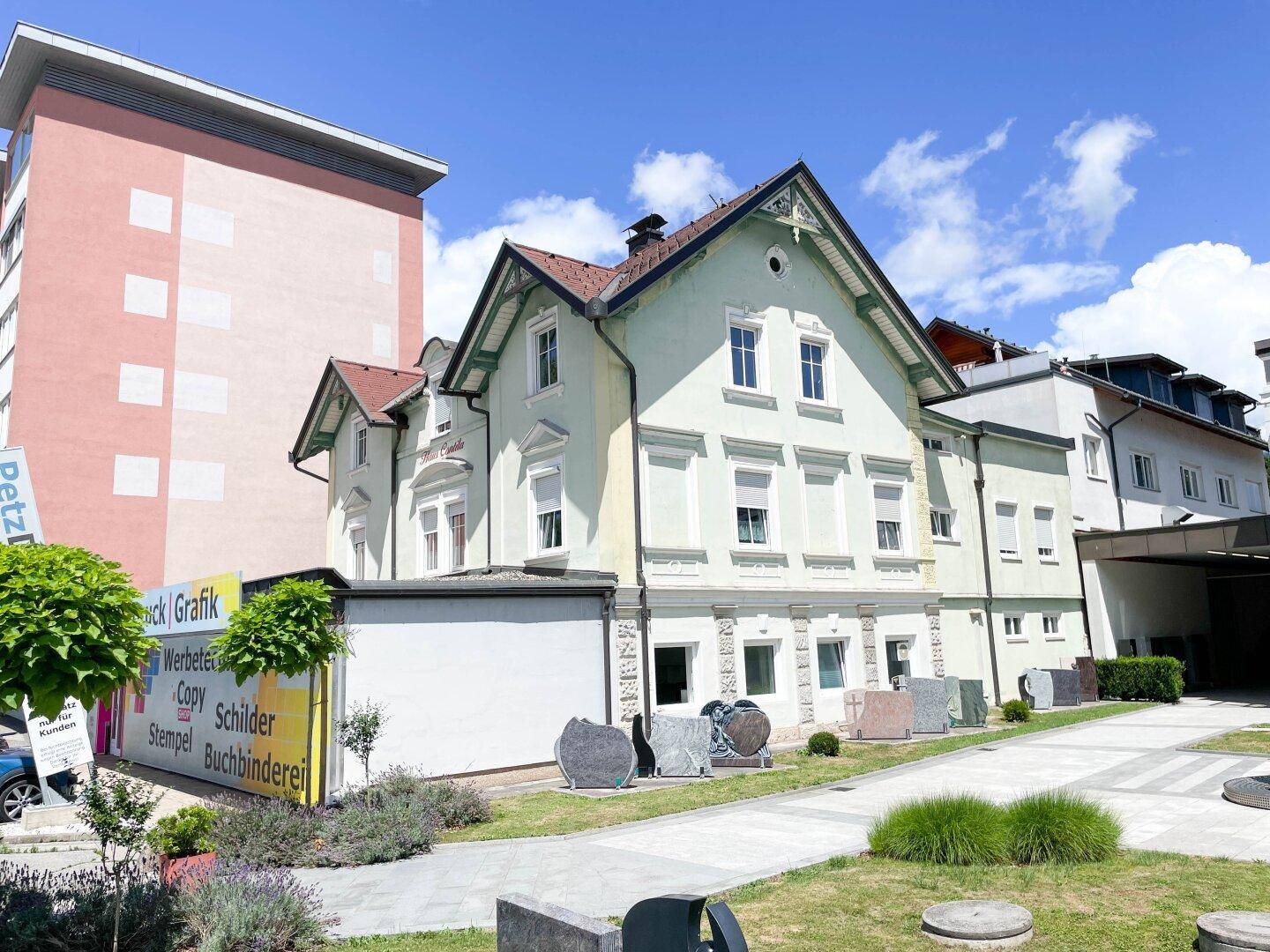 Historisches Gebäude mit gepflegter Fassade und kleinem Vorgarten unter blauem Himmel.