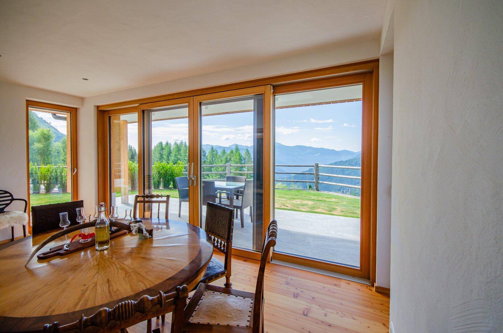 Gemütlicher Essbereich mit Holztisch und Stühlen, großen Fenstern und Panoramablick auf die Berge.