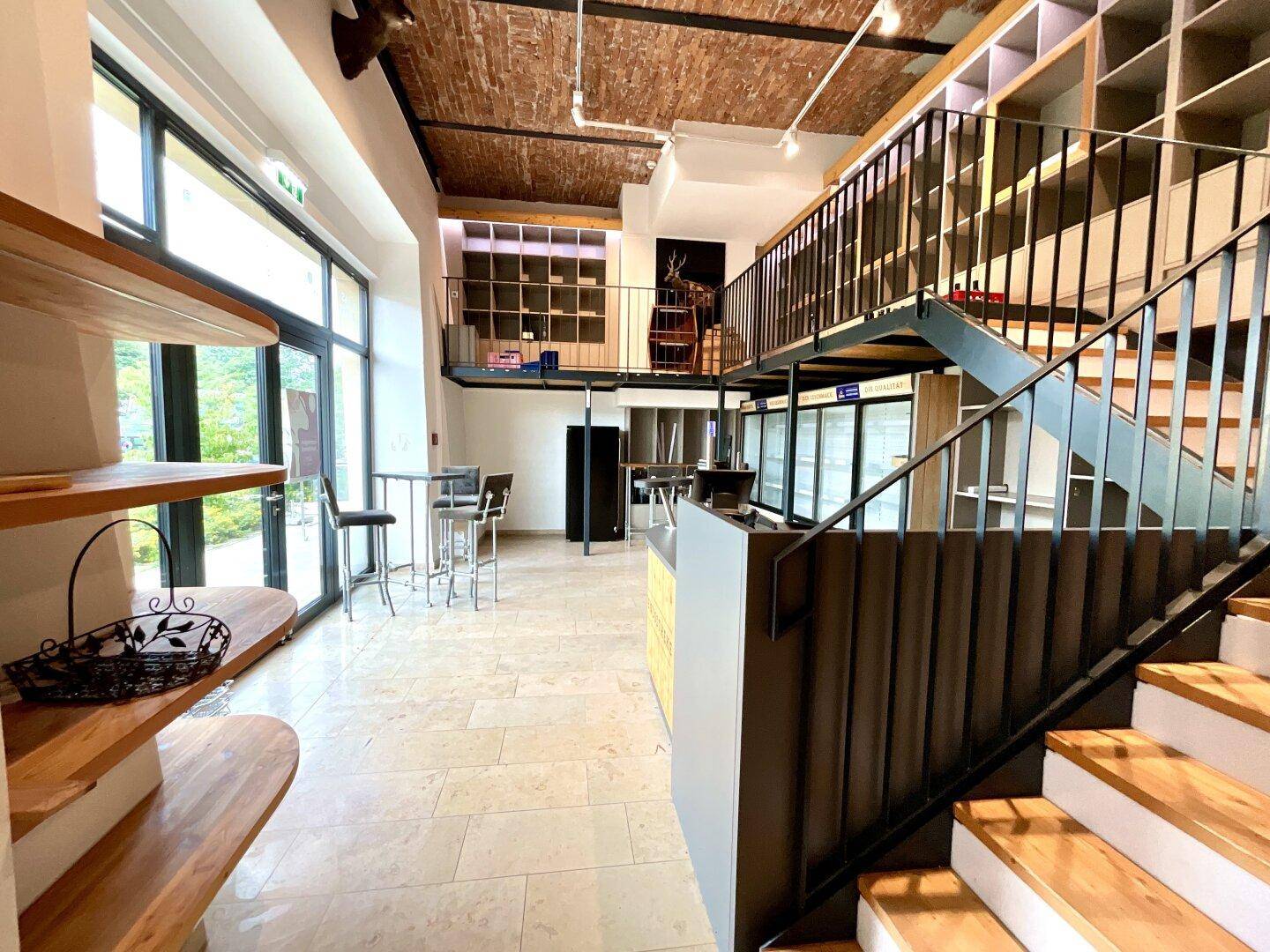 Offener Verkaufsbereich mit Holzregalen, Fliesenboden und einer Treppe zur oberen Galerieebene.