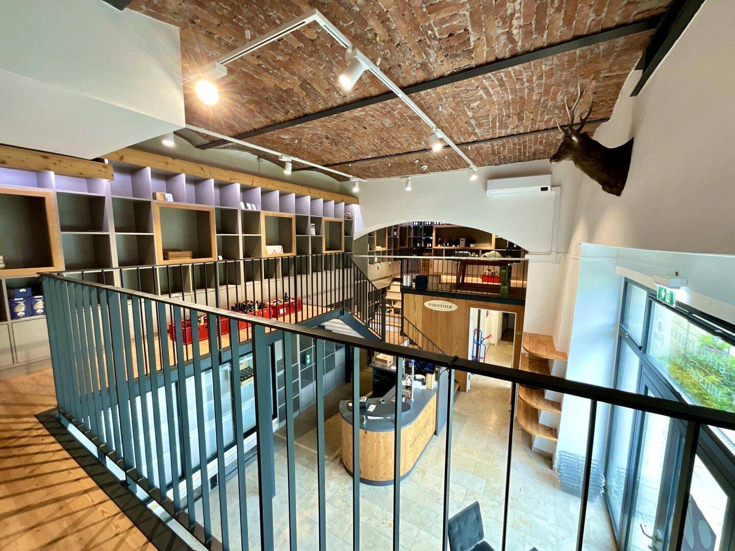 Heller Verkaufsraum mit Ziegelgewölbedecke, Fliesenboden und einer modernen Galerie mit schwarzem Metallgeländer.