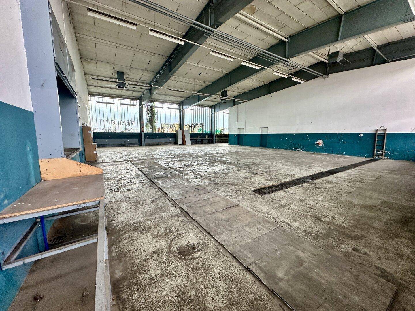 Geräumige Industriehalle mit hohen Decken, Betonboden und großen Fenstern, bereit zur Nutzung.