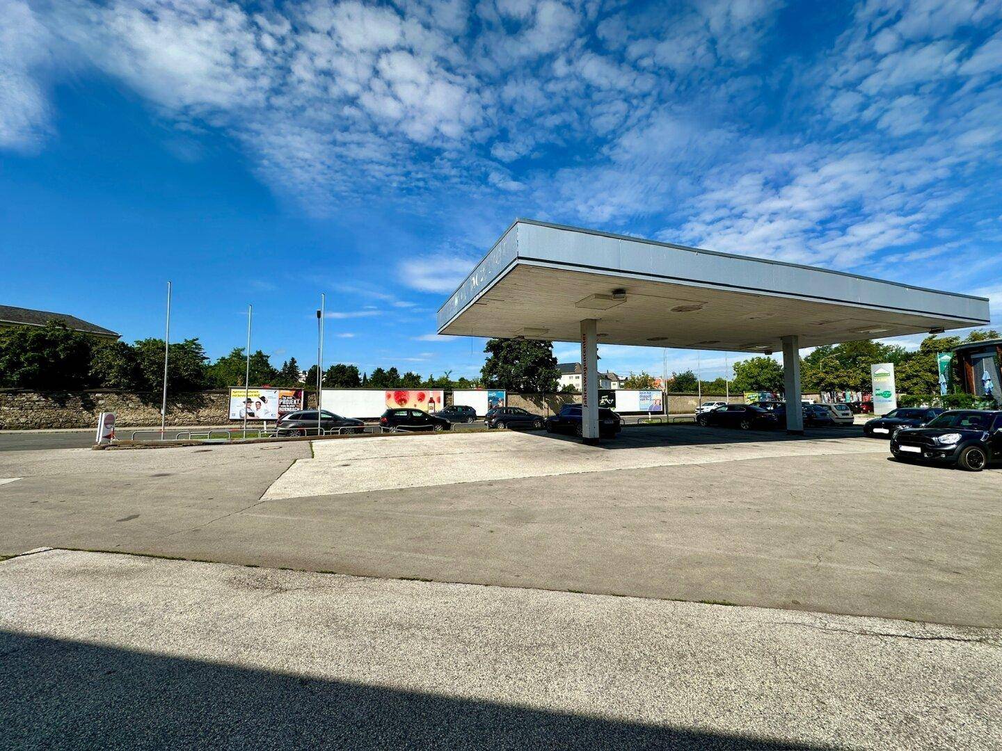 Außenbereich einer Tankstelle mit Überdachung und großzügigen Parkmöglichkeiten unter blauem Himmel.