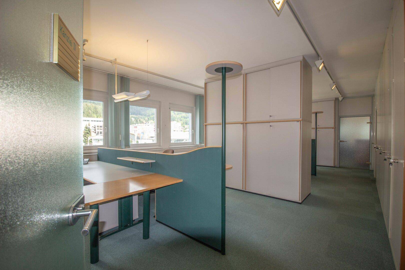 Blick durch ein Großraumbüro mit modularen Arbeitsplätzen und einem Flur, der zu weiteren Räumen führt.
