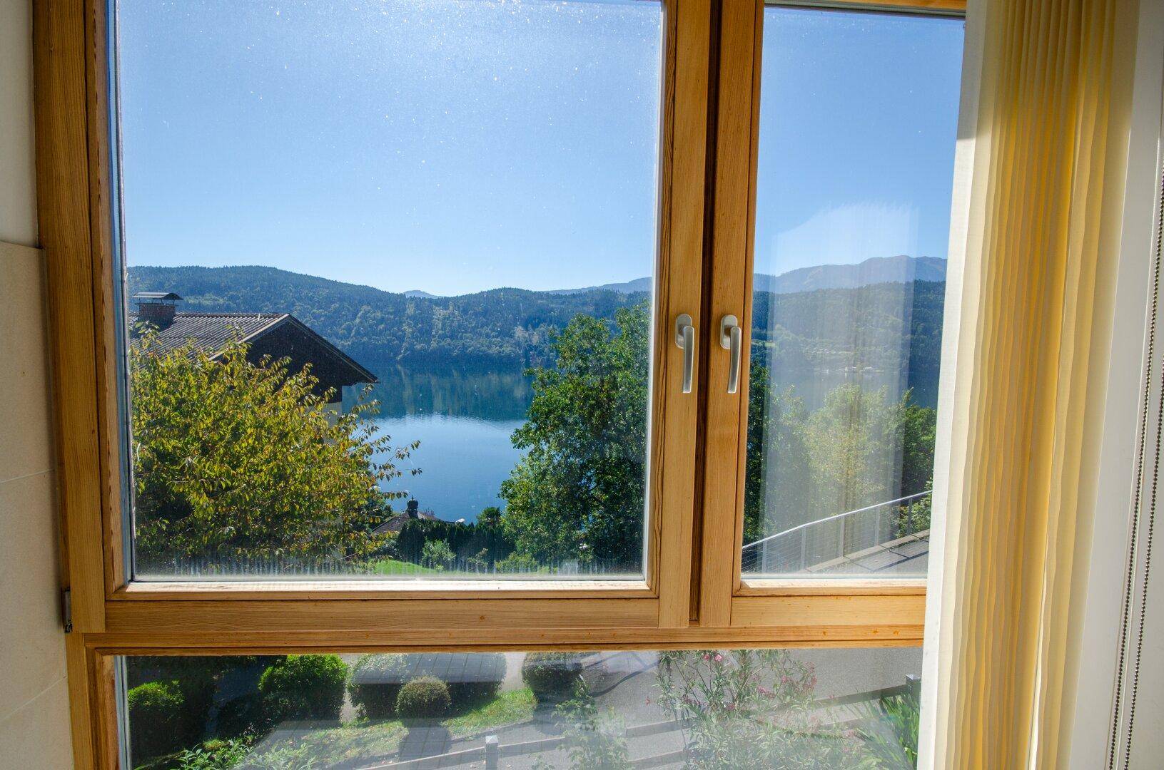 Fensterblick auf den glitzernden See und die bewaldeten Hügel unter strahlend blauem Himmel.