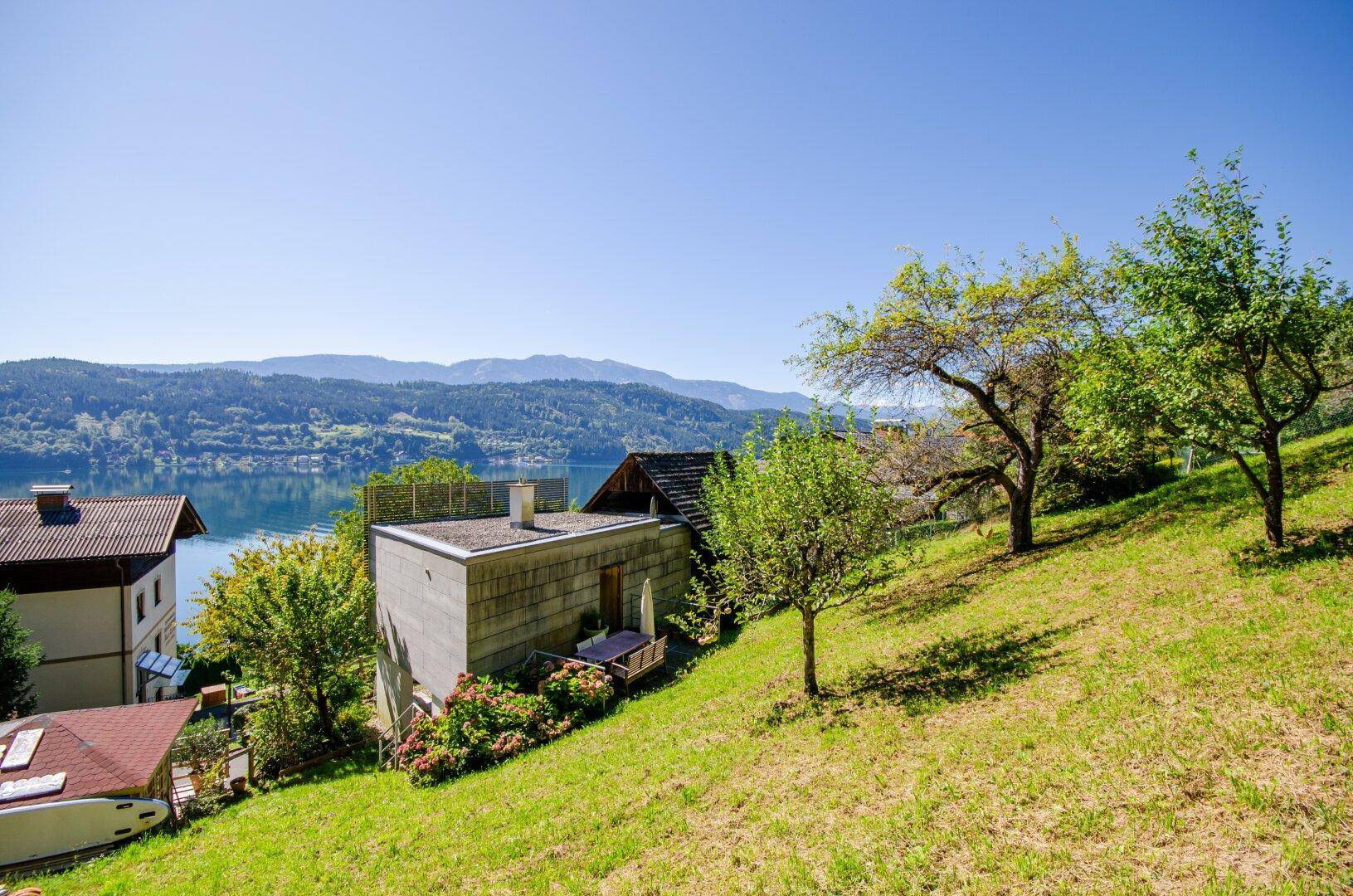 Weitläufiger Blick auf das Anwesen, den See und die umliegende Hügellandschaft unter blauem Himmel.