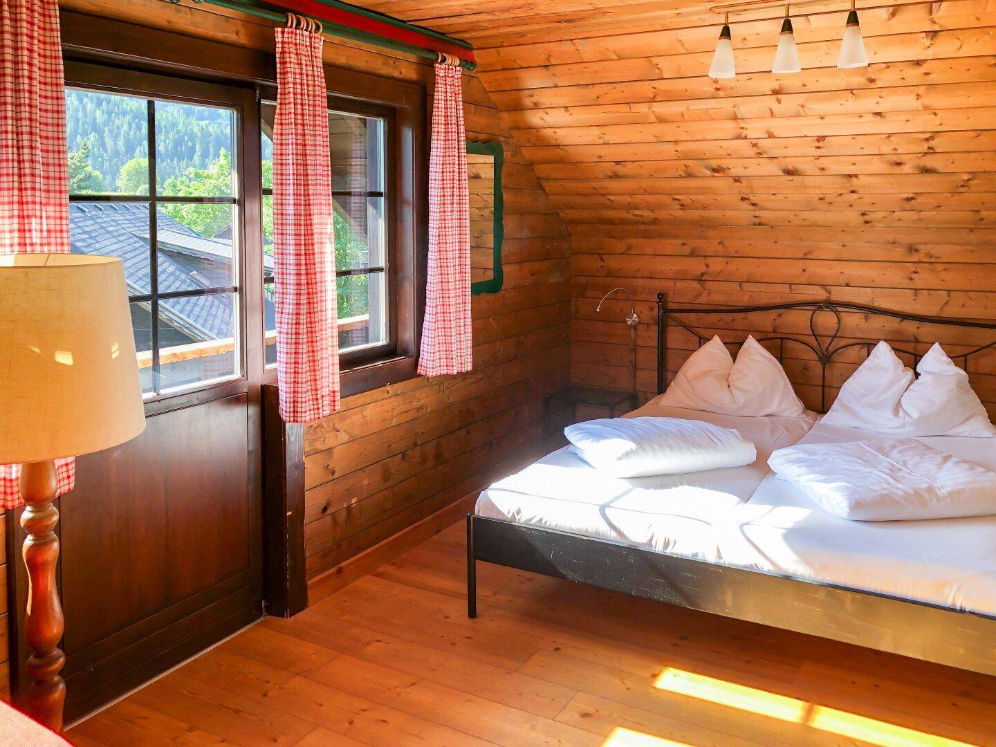 Helles Schlafzimmer mit Holztäfelung, Doppelbett und Zugang zu einem kleinen Balkon.