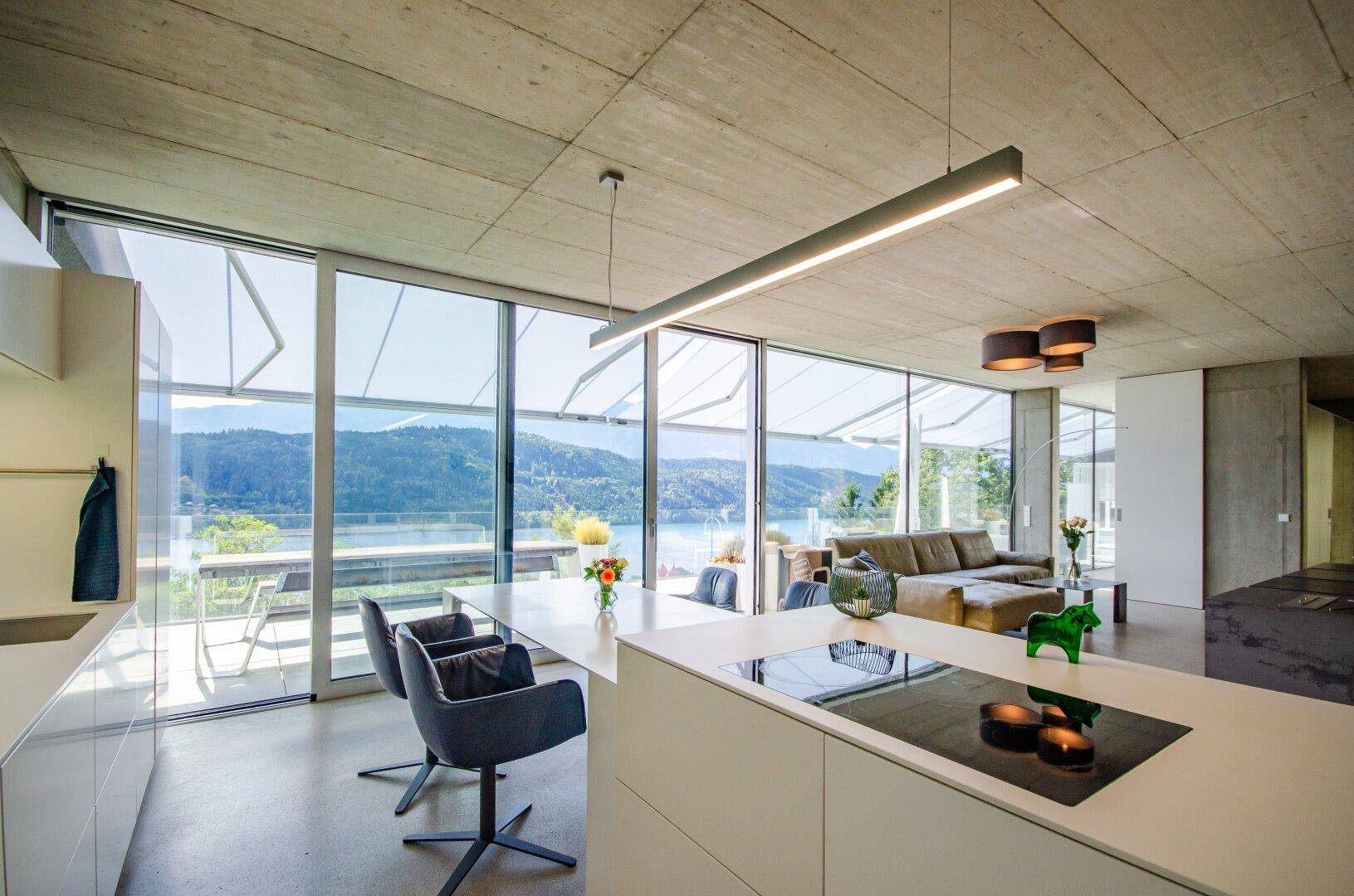 Moderne offene Küche mit Kochinsel, integriertem Essbereich und Panoramablick auf den See.