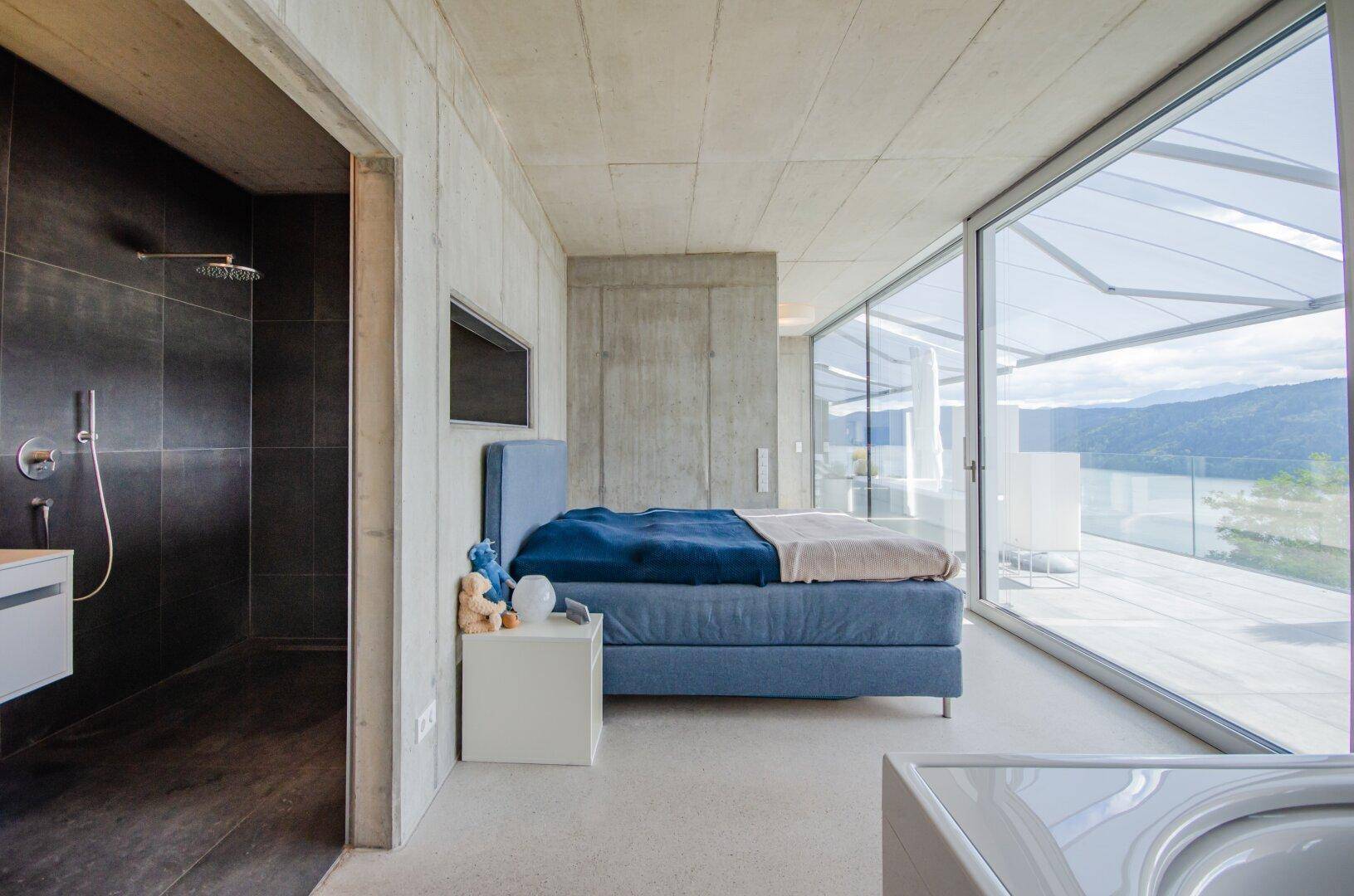 Schlafzimmer mit direktem Zugang zur Terrasse, Seeblick und angrenzendem Duschbereich.