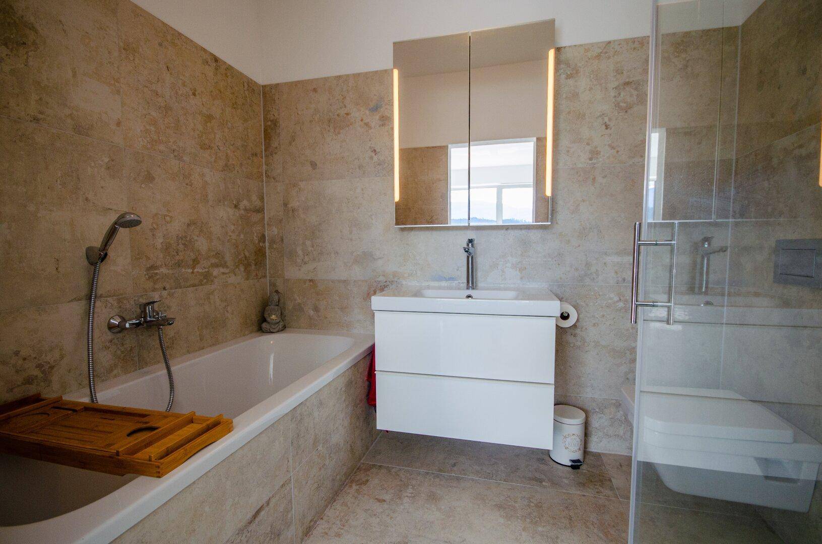 Modernes Badezimmer mit Badewanne, separater Dusche und eleganten Fliesen in Natursteinoptik.