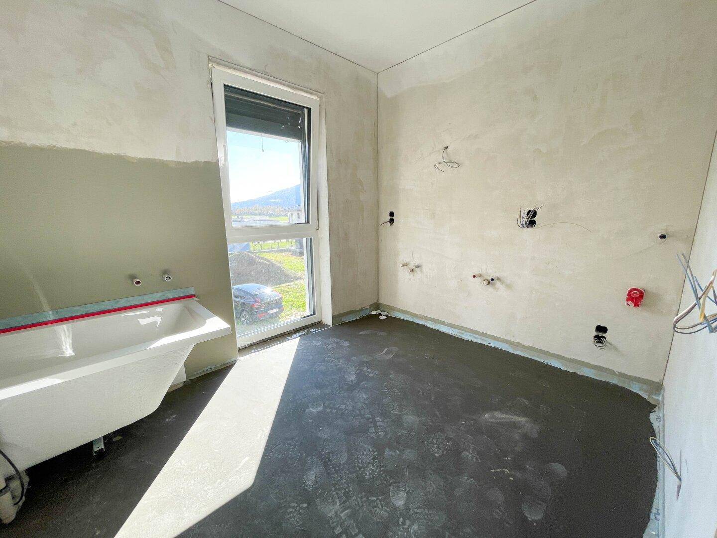 Badezimmer im Rohbau mit Badewanne und großem Fenster, bereit für die Fertigstellung.