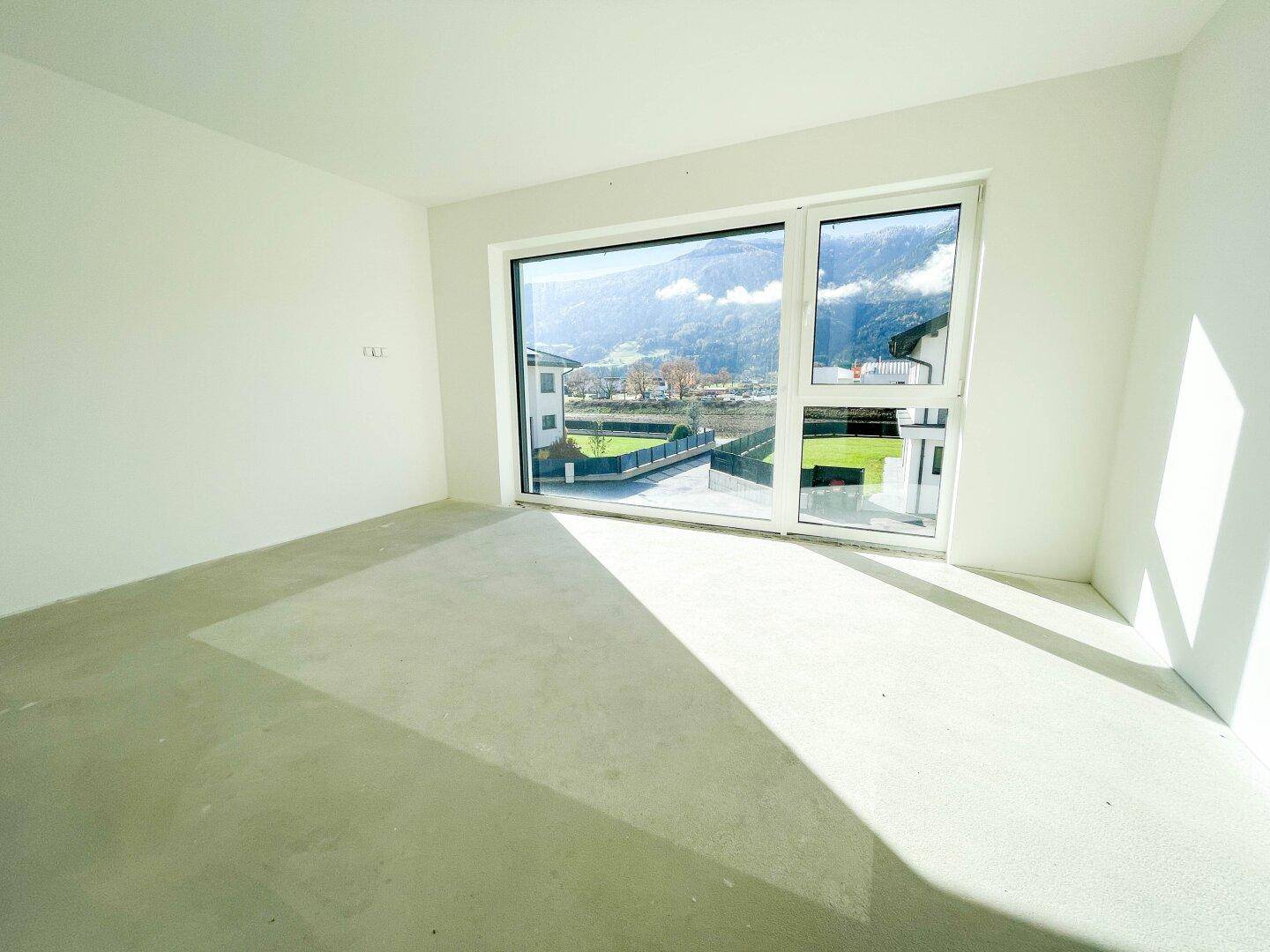 Leerer Raum im Rohbau mit großem Fenster und weitem Blick auf die Berge.