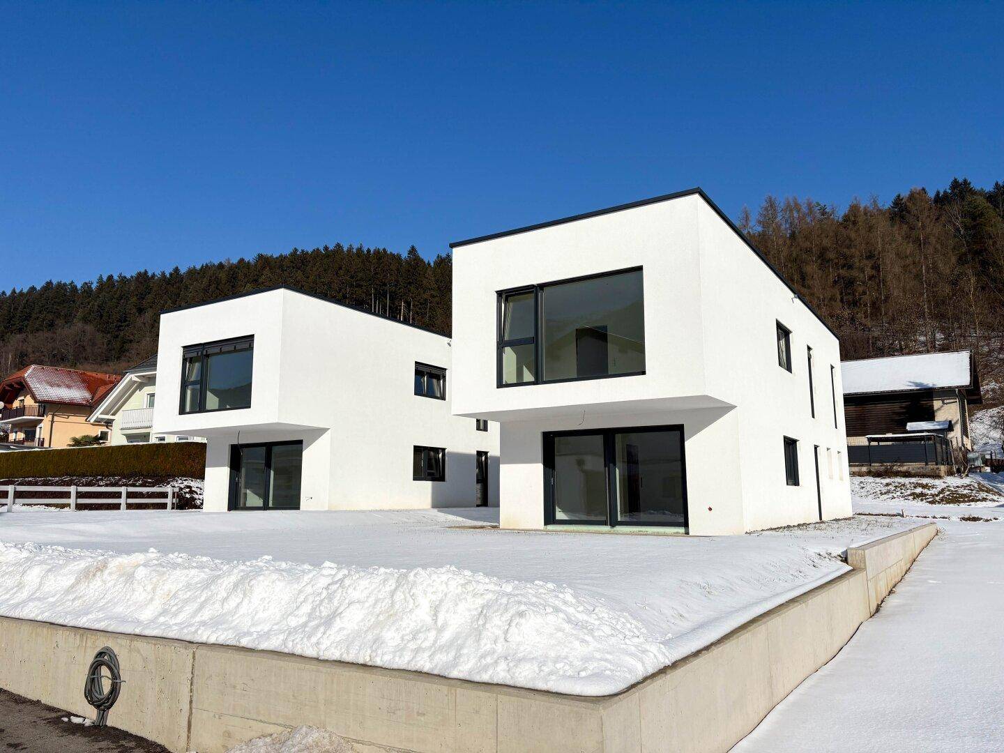 Ansicht von zwei modernen weißen Häusern mit großen Fenstern in einer verschneiten Landschaft.