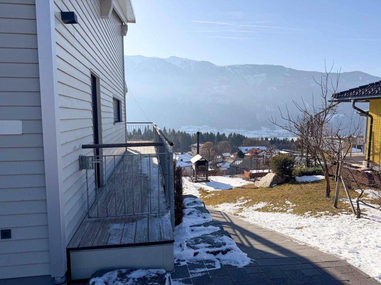 Seitenansicht des Hauses mit kleinem Balkon und weitem Blick auf die schneebedeckte Landschaft und Berge.