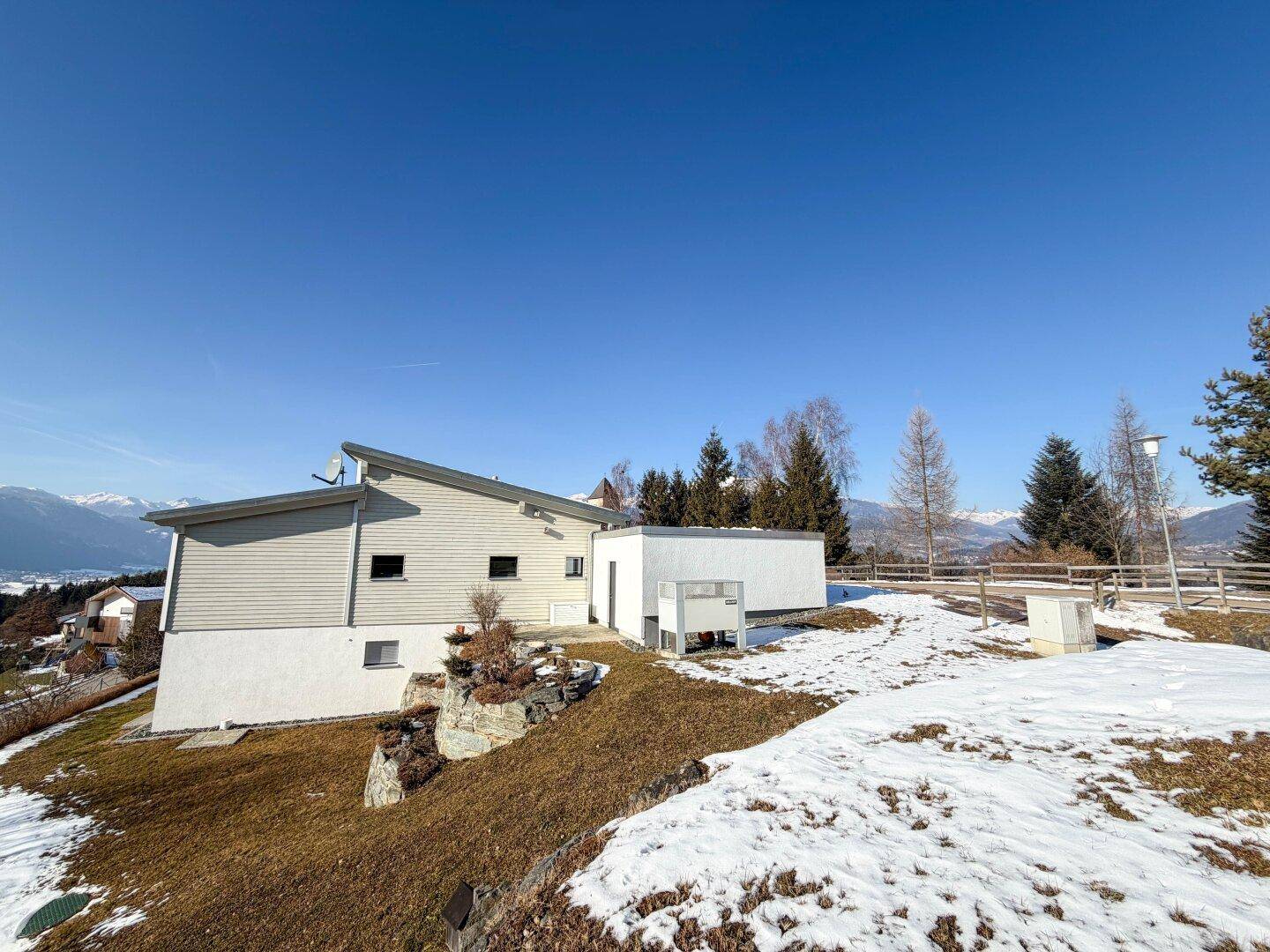 Rückansicht des modernen Hauses mit Schrägdach und weitläufigem Grundstück in alpiner Umgebung.