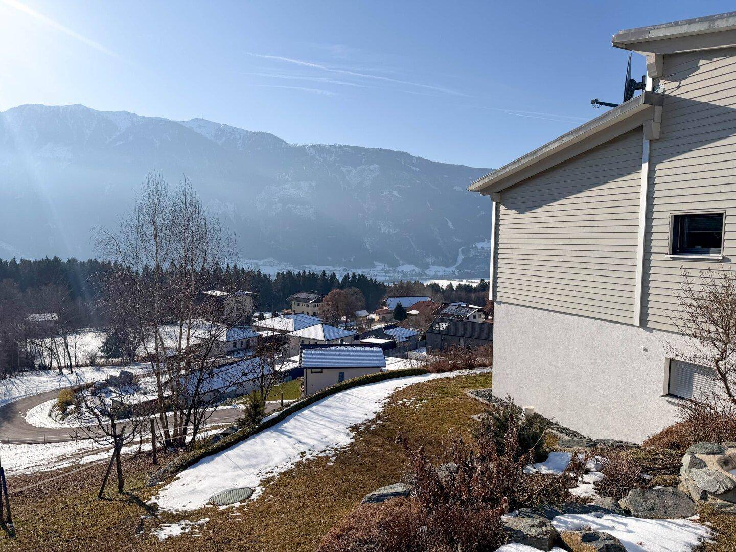 Seitenansicht des Hauses mit Blick auf die verschneite Landschaft, umliegende Häuser und die Bergkette.