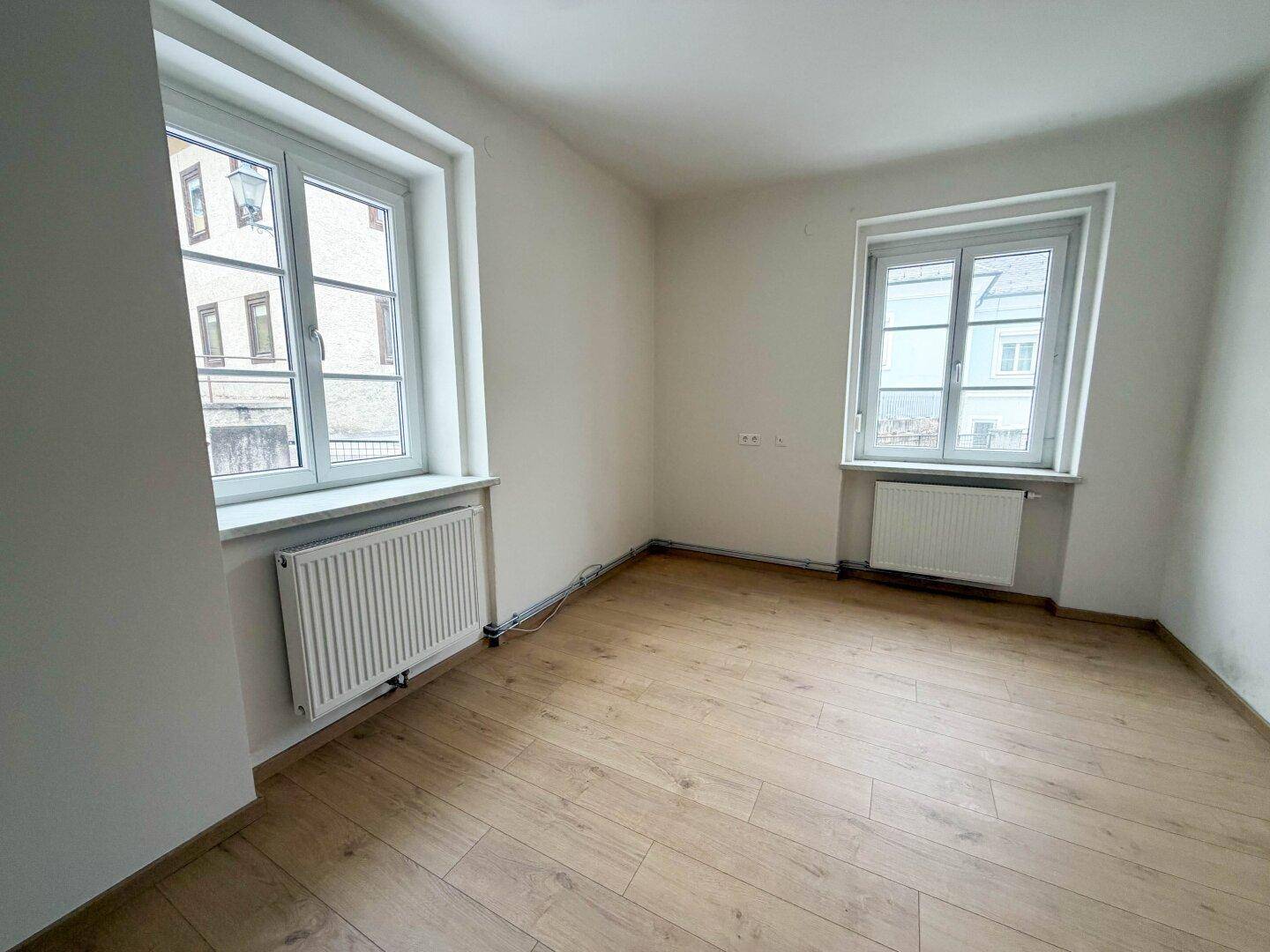 Helles Schlafzimmer mit zwei Fenstern und Heizkörpern, ausgestattet mit Laminatboden und viel Tageslicht.