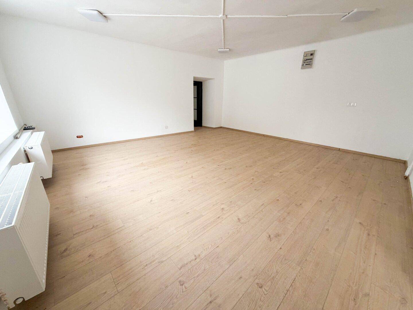 Geräumiger, heller Raum mit Holzboden und weiß gestrichenen Wänden, bereit für individuelle Gestaltung.