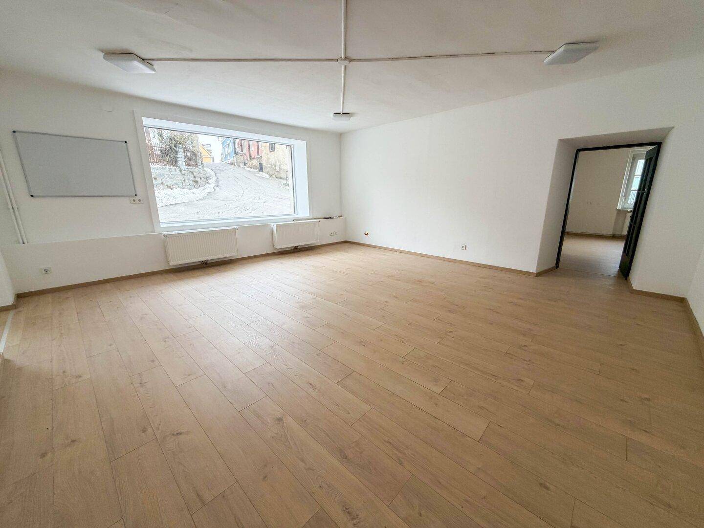 Großer, leerer Raum mit Laminatboden und Blick auf die schneebedeckte Straße, bietet viel Tageslicht.