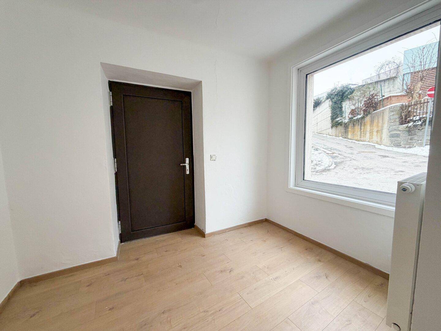 Kleiner Raum mit dunkler Tür, großem Fenster und Blick auf die schneebedeckte Straße, vielseitig nutzbar.