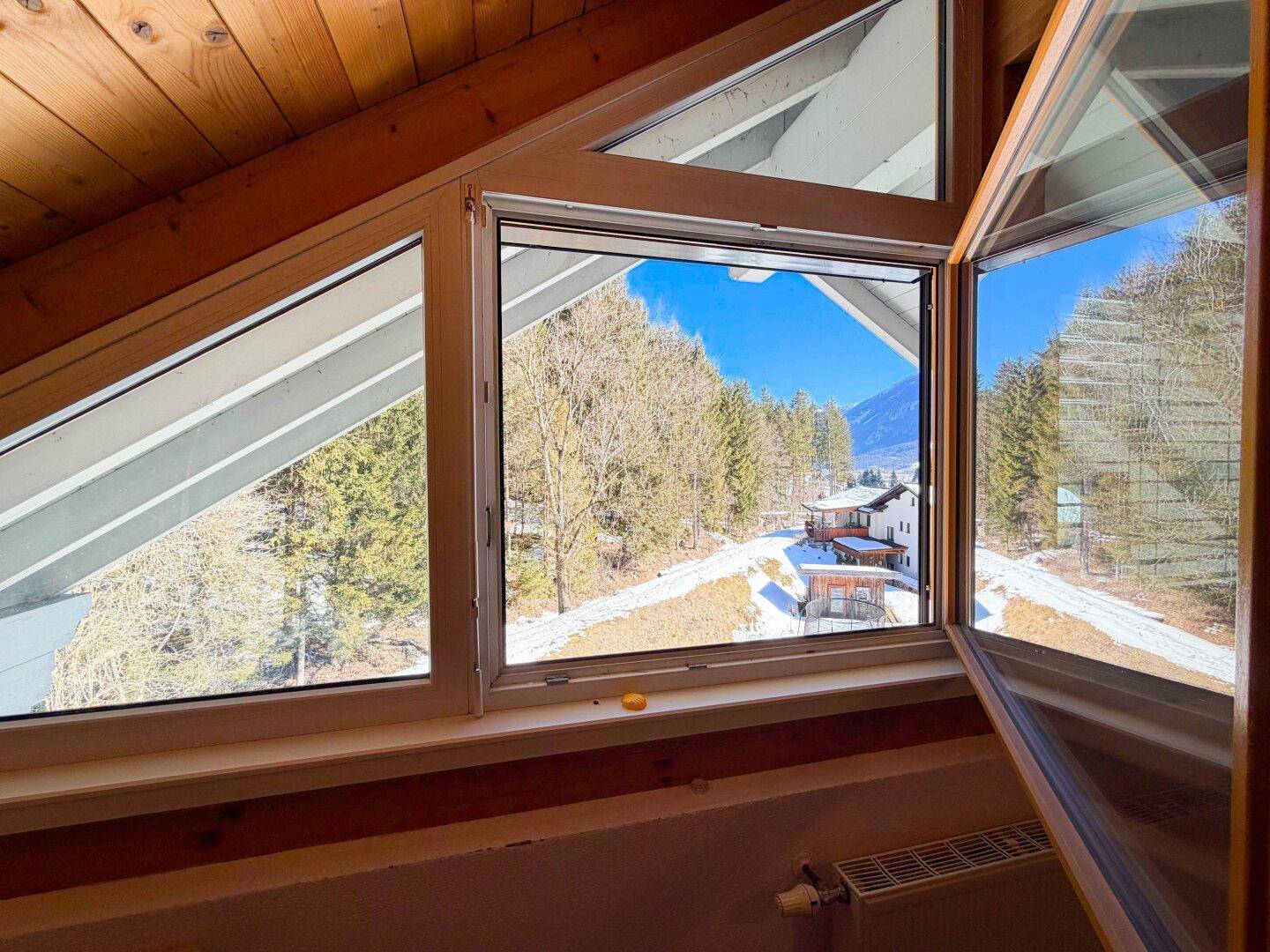 Weitblick aus dem Dachfenster auf die schneebedeckte Landschaft und die umliegenden Berge.