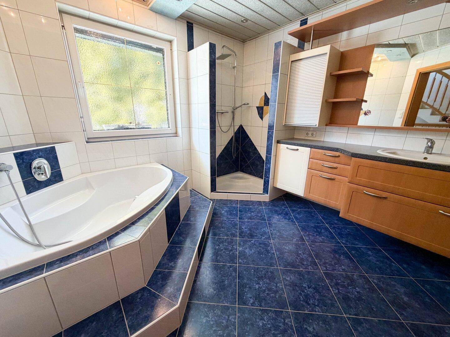 Badezimmer mit blauen und weißen Fliesen, Badewanne, Dusche und Einzelwaschbecken.