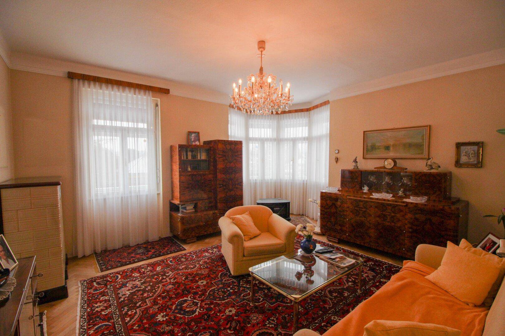 Geräumiges Wohnzimmer mit antiken Holzmöbeln, Teppich und großem Kronleuchter.